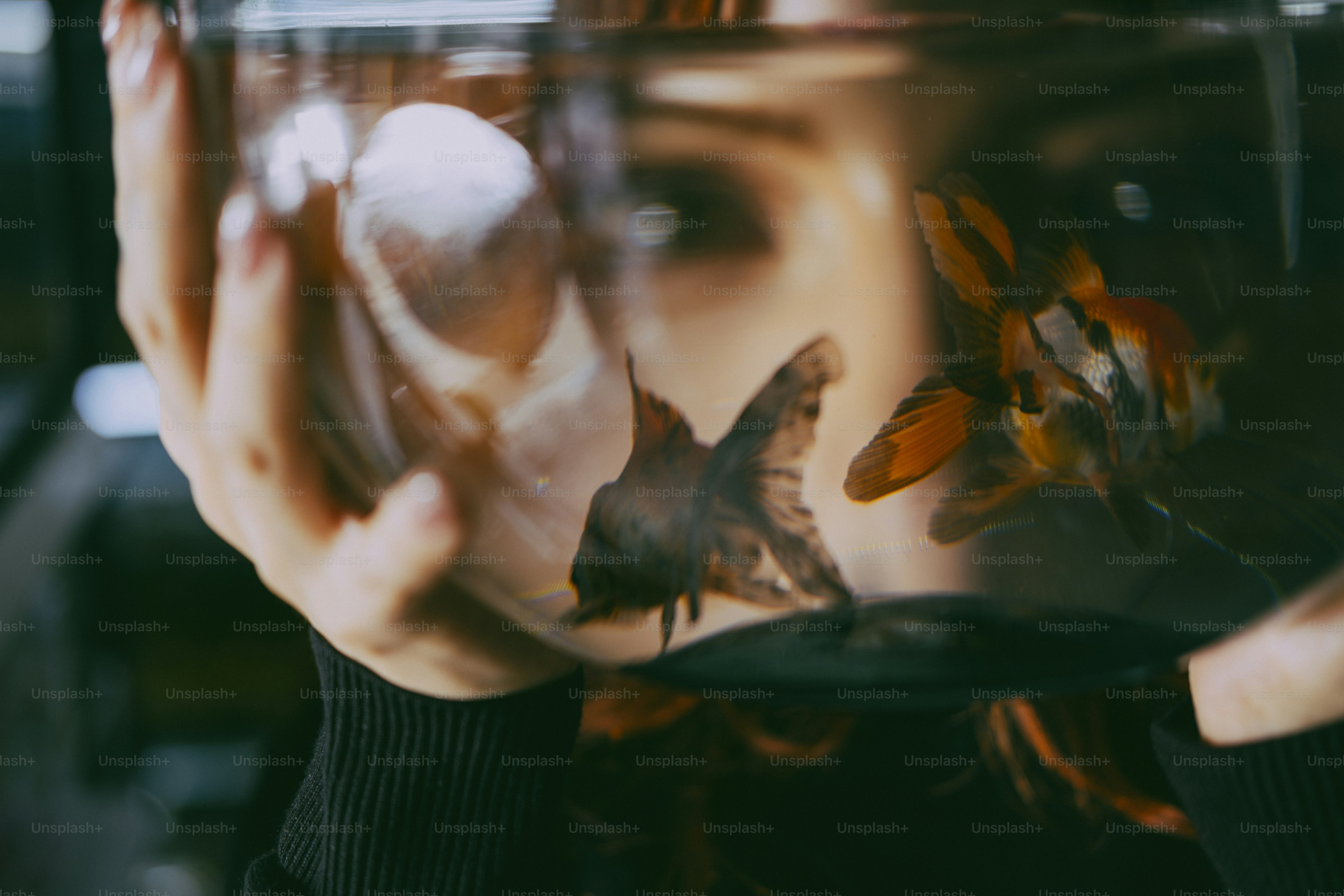 A person holding a glass bowl containing two goldfish in front of their face