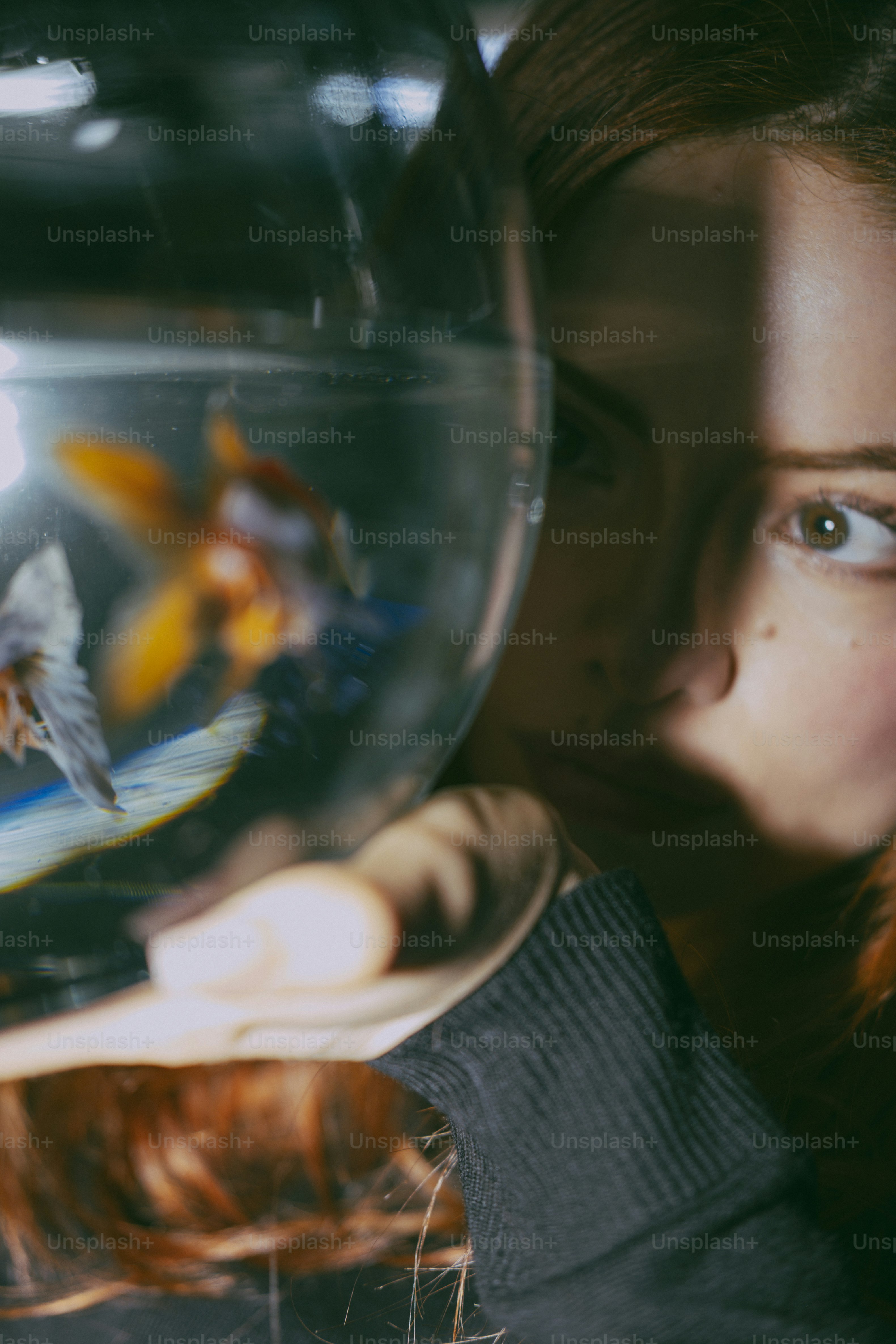 A woman looking through a glass fishbowl containing a goldfish