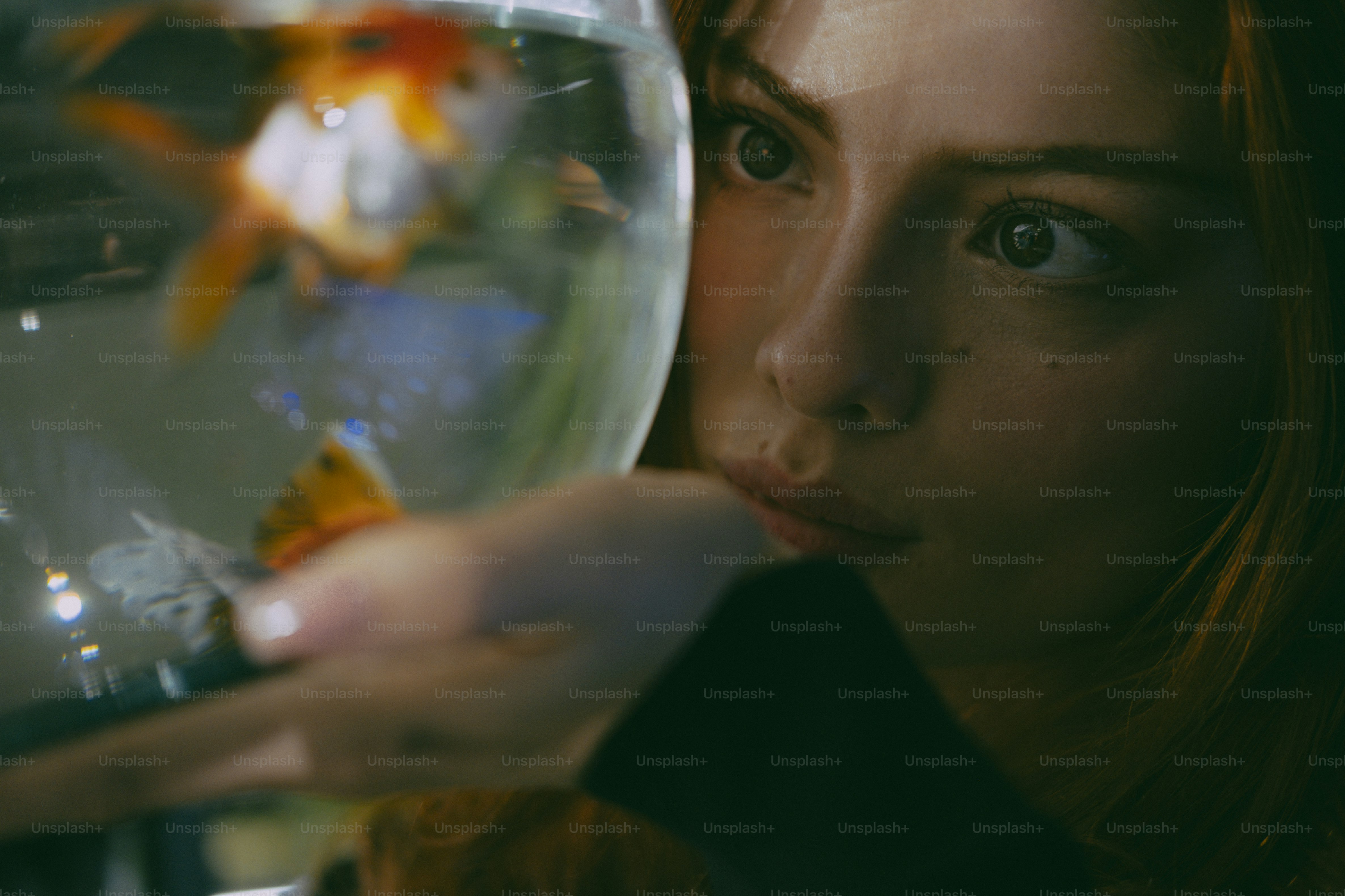A woman looking at a goldfish swimming in a glass bowl
