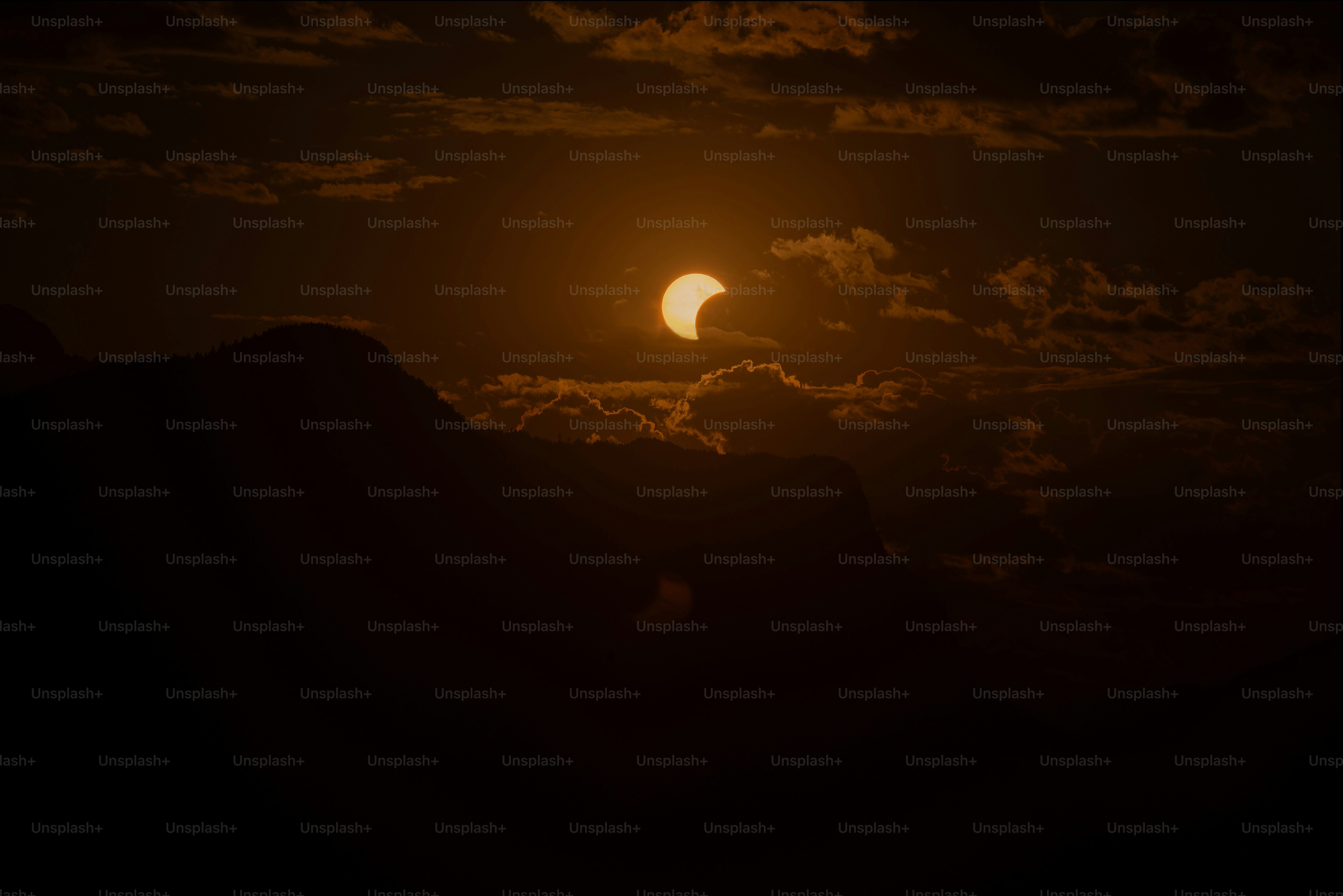 A partial solar eclipse above a dark mountain silhouette in a cloudy sky