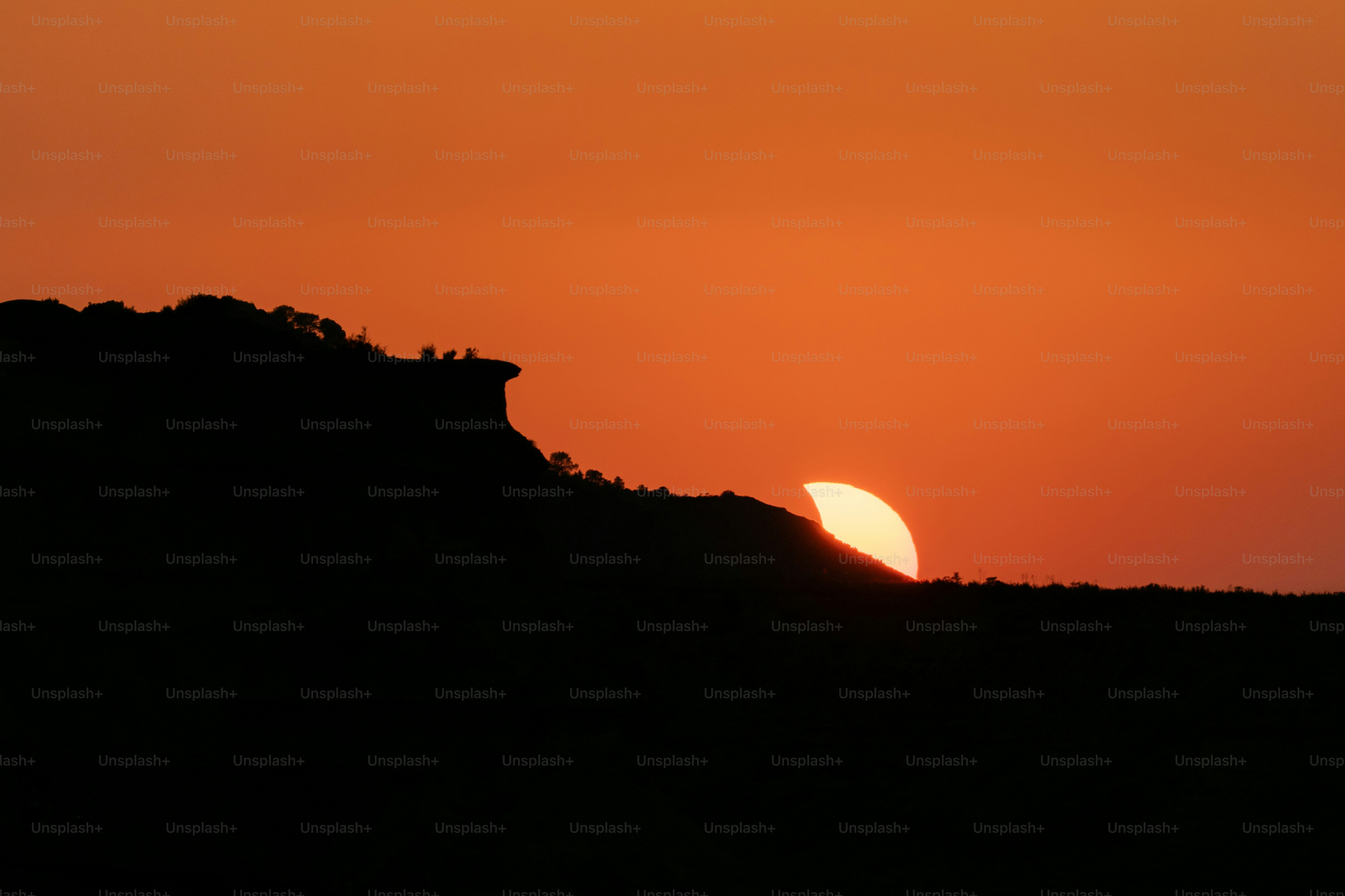 A dark silhouette of a ridge against a bright orange sky