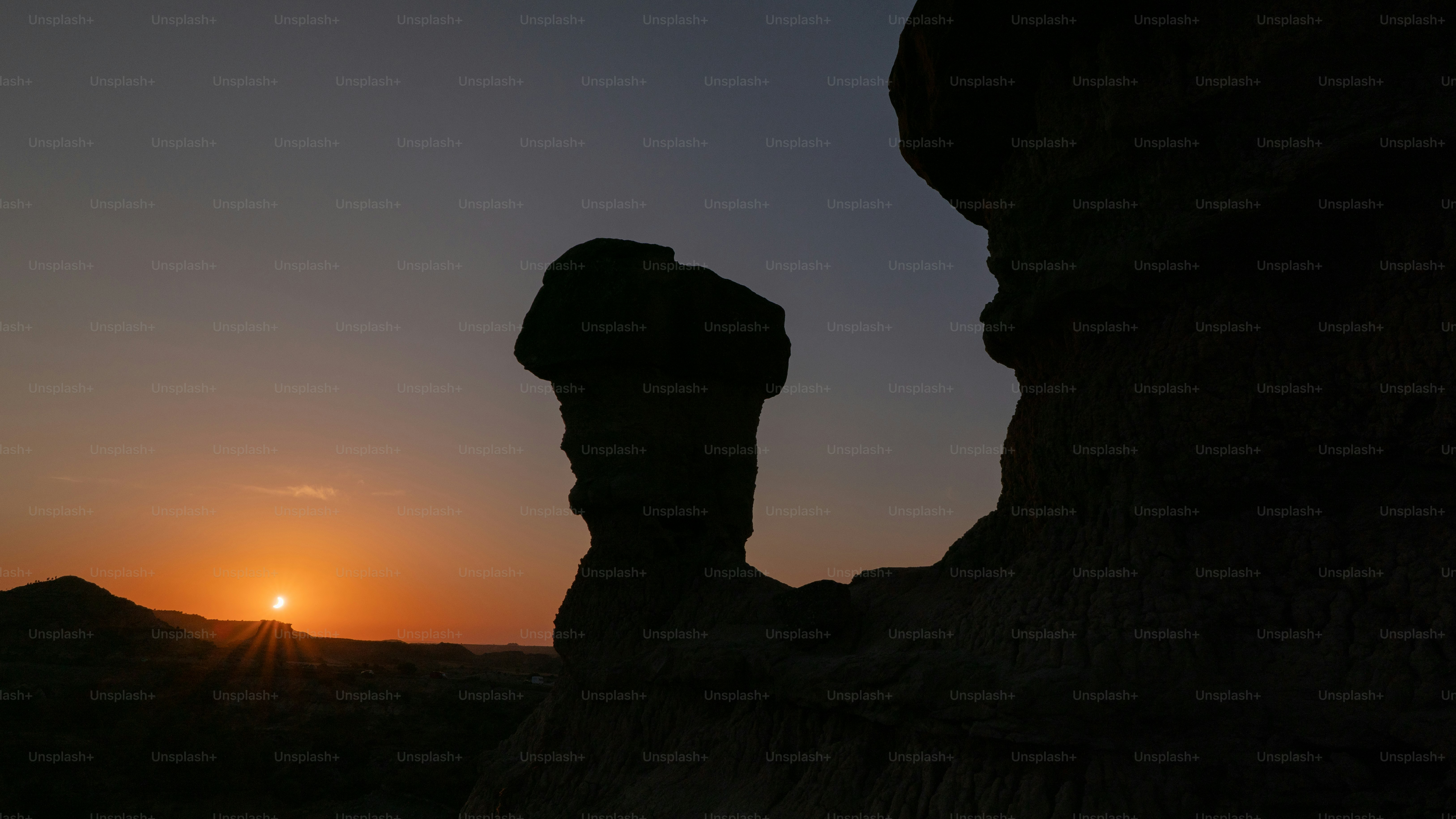 A rock formation in silhouette against a warm orange sky with low sun