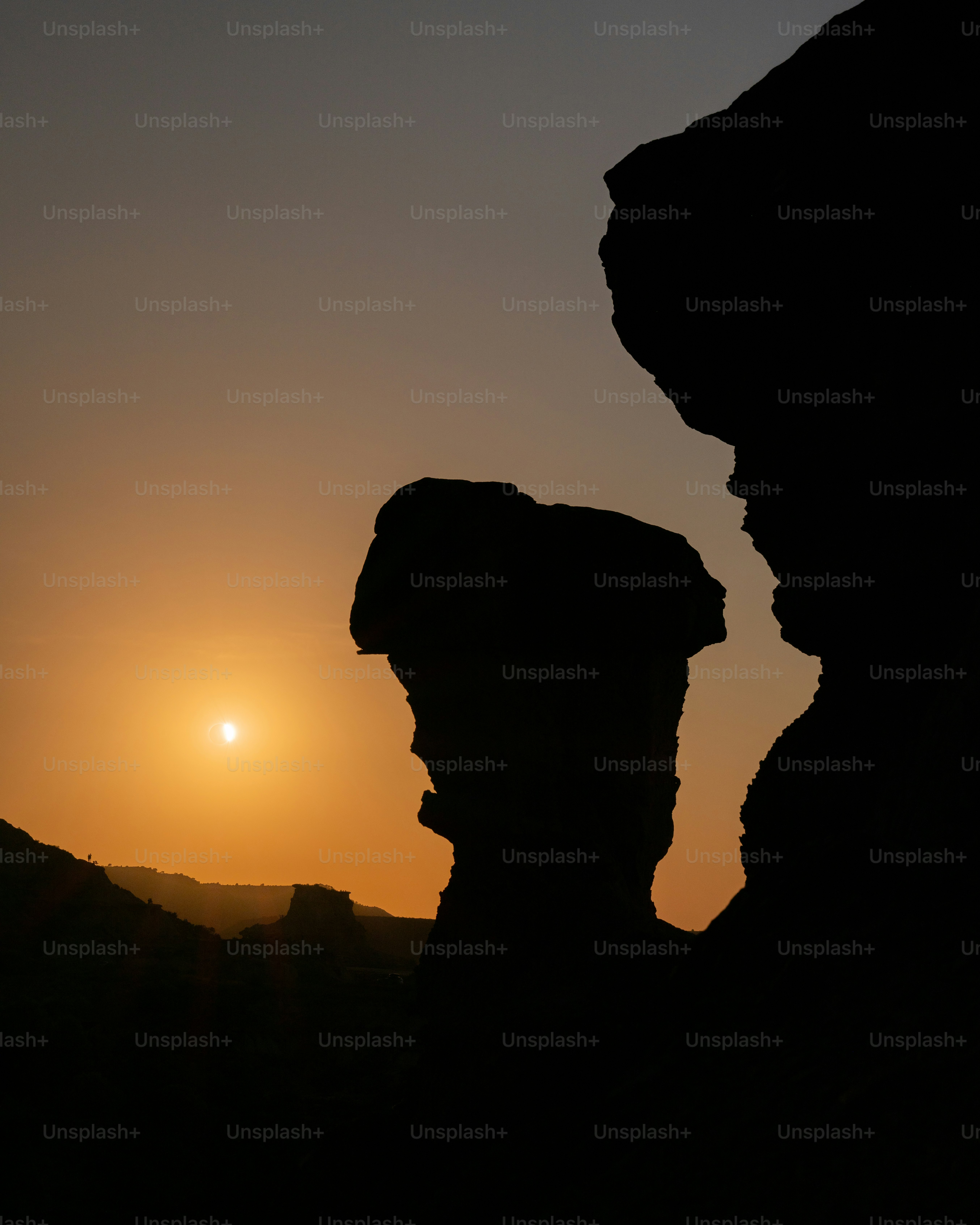 Silhouetted rock formations against a warm orange sky with a low sun