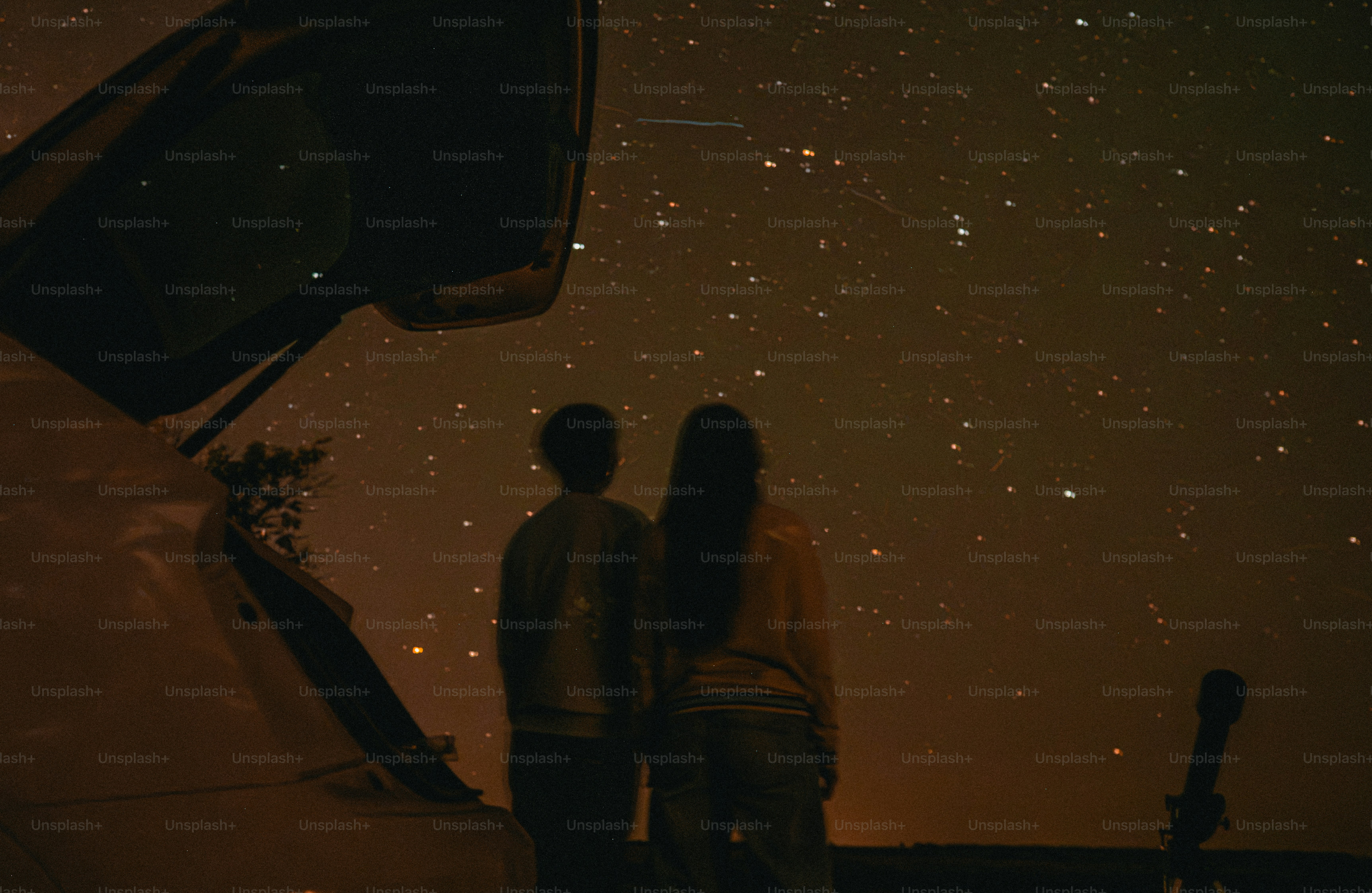 Two people in silhouette looking at a starry night sky beside a car