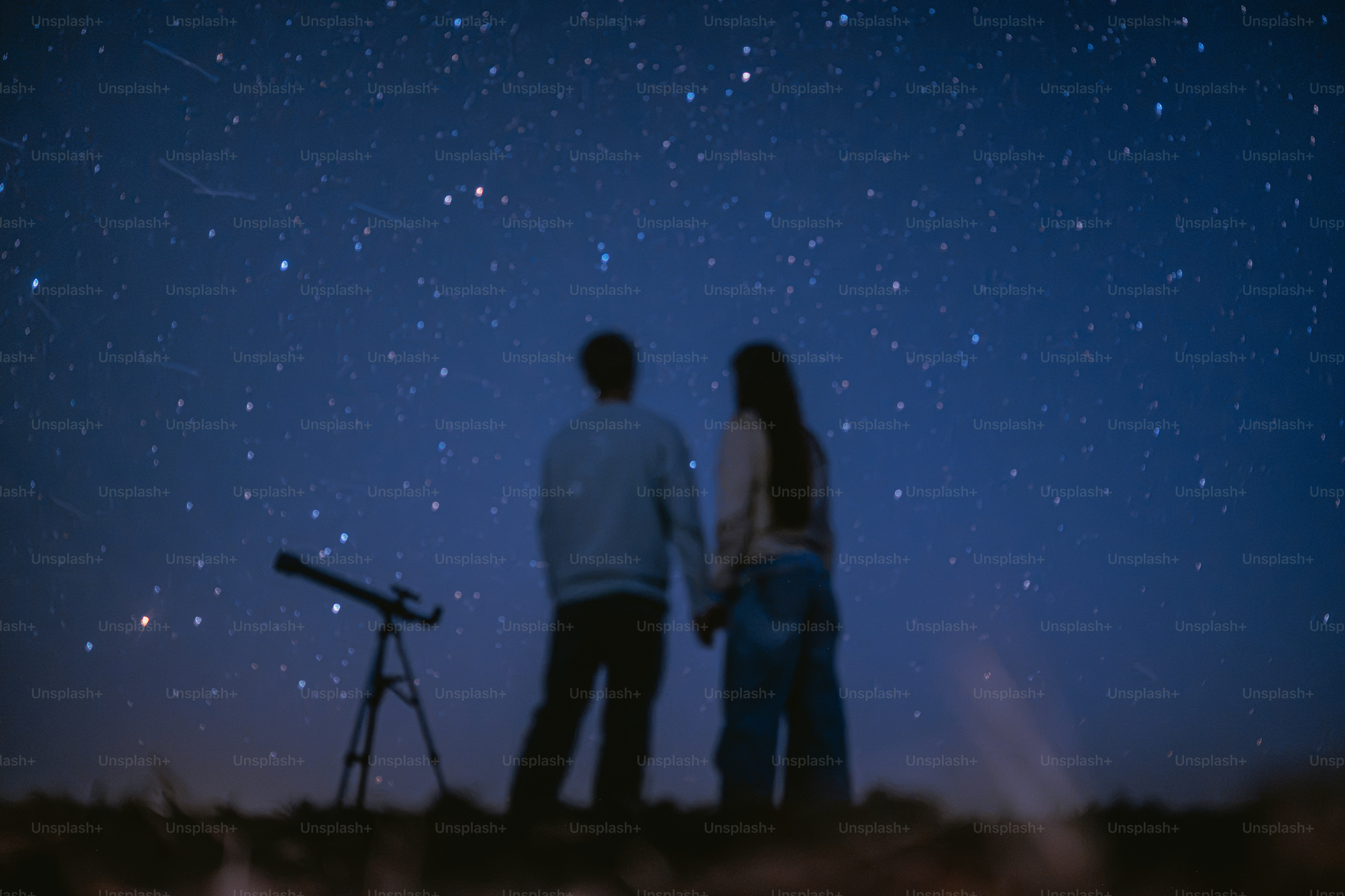 Two people holding hands while looking at a starry night sky with a telescope