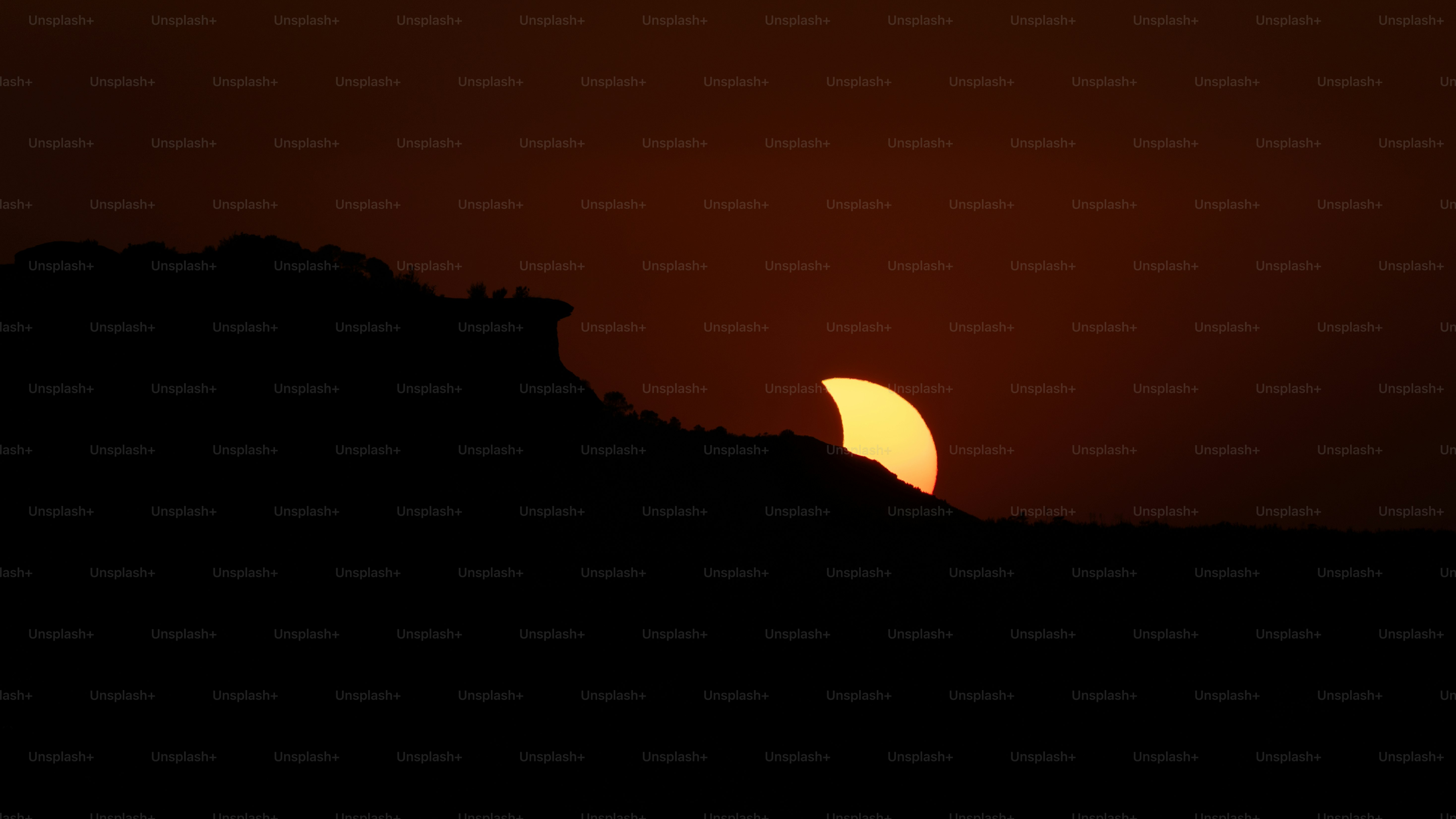 A partial solar eclipse behind a dark silhouetted mountain ridge