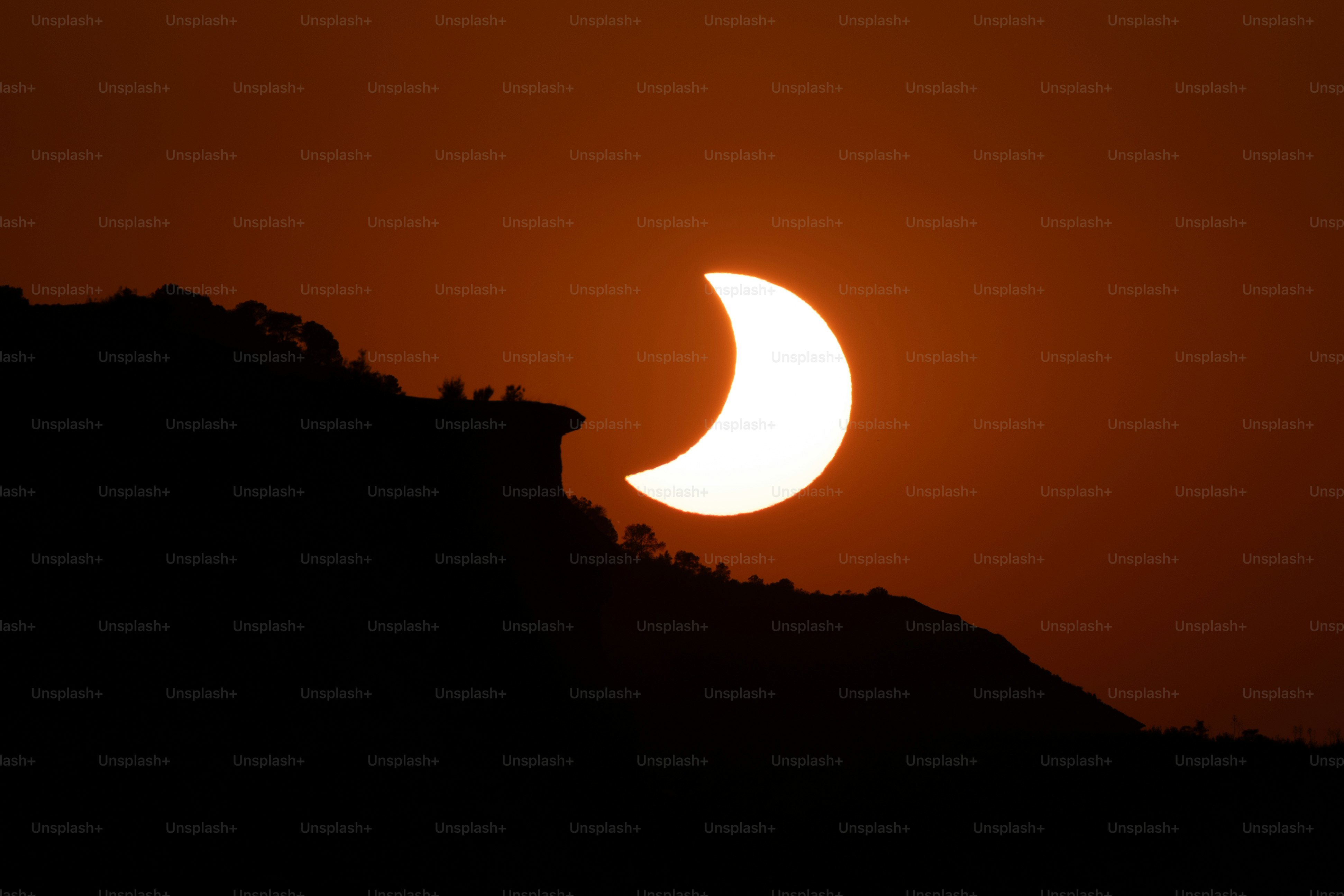 A partial solar eclipse above a dark silhouetted mountain ridge at golden hour