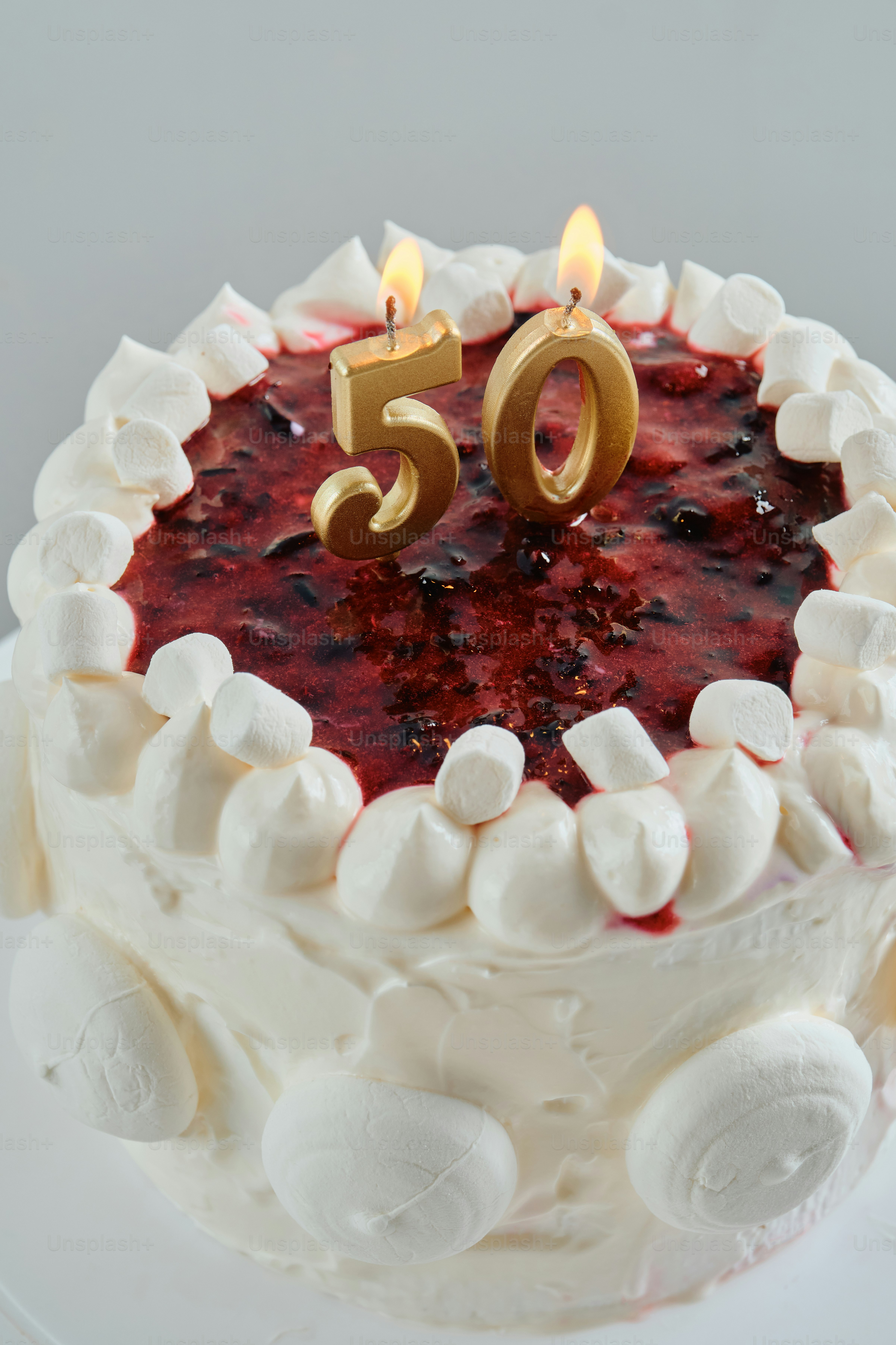 Un gâteau avec glaçage blanc, confiture de baies et deux bougies dorées allumées