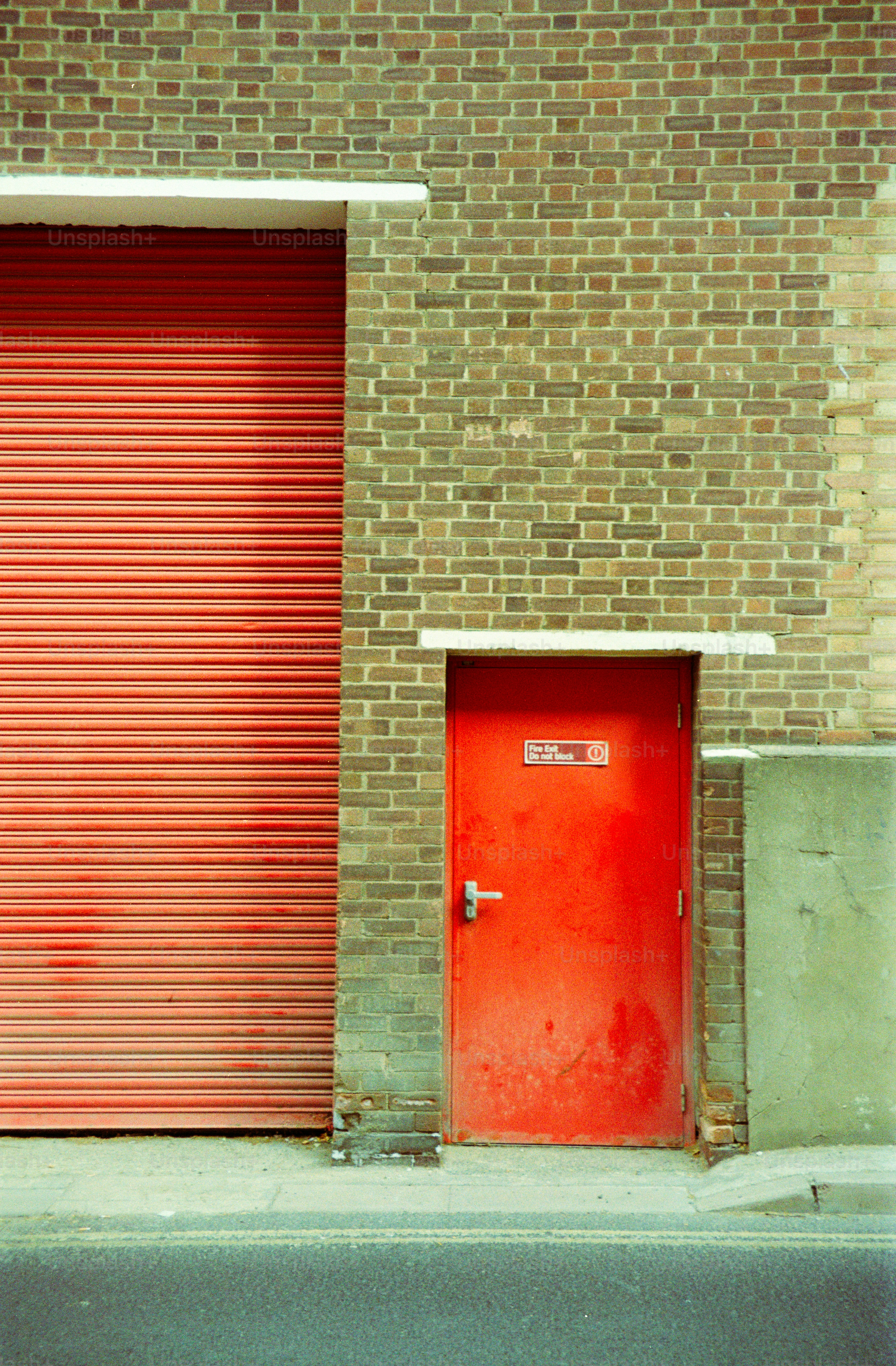 A red metal door and a large rolling shutter on a brick building.