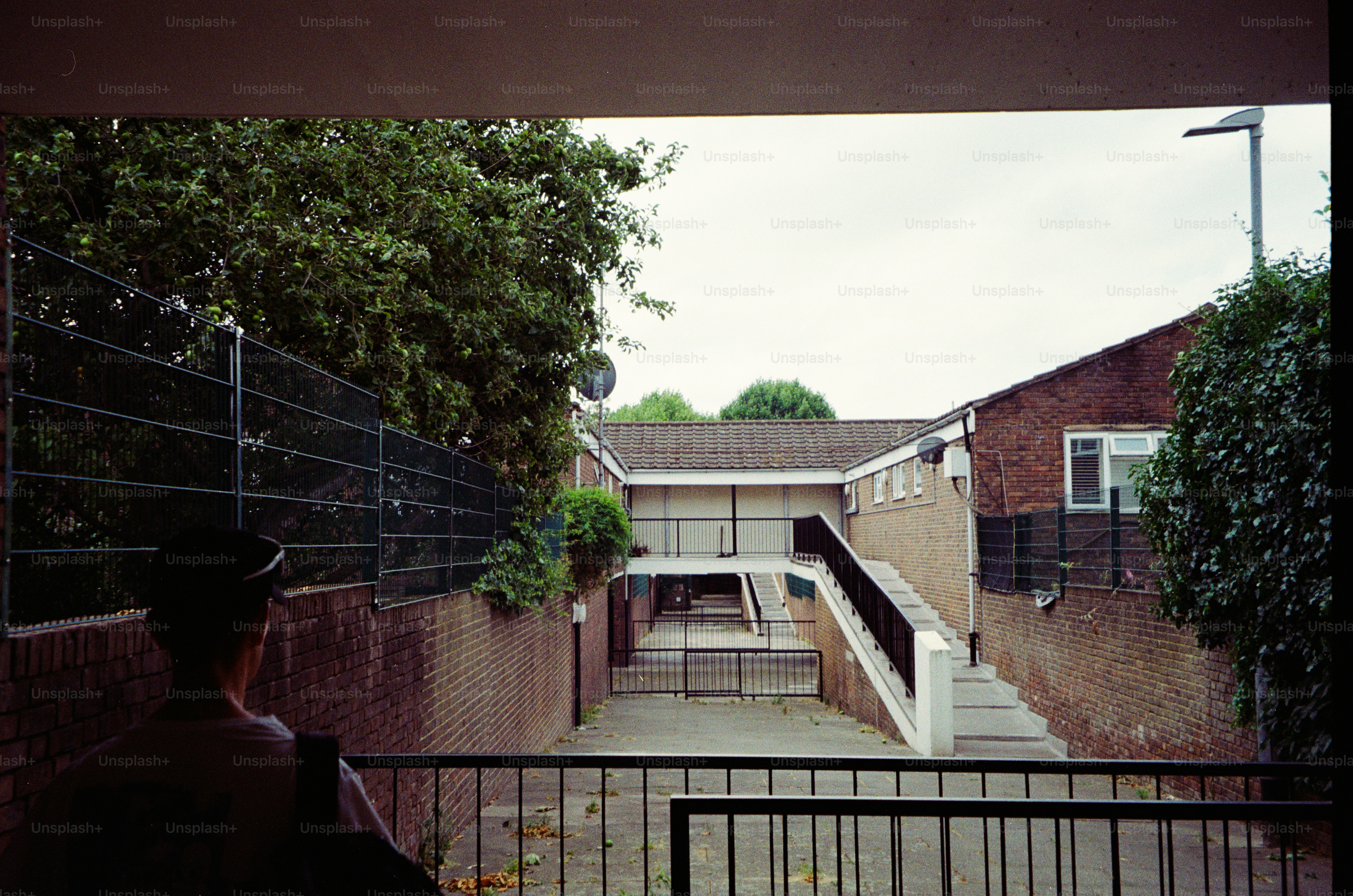 A person in a cap looking toward a brick building with an outdoor staircase.