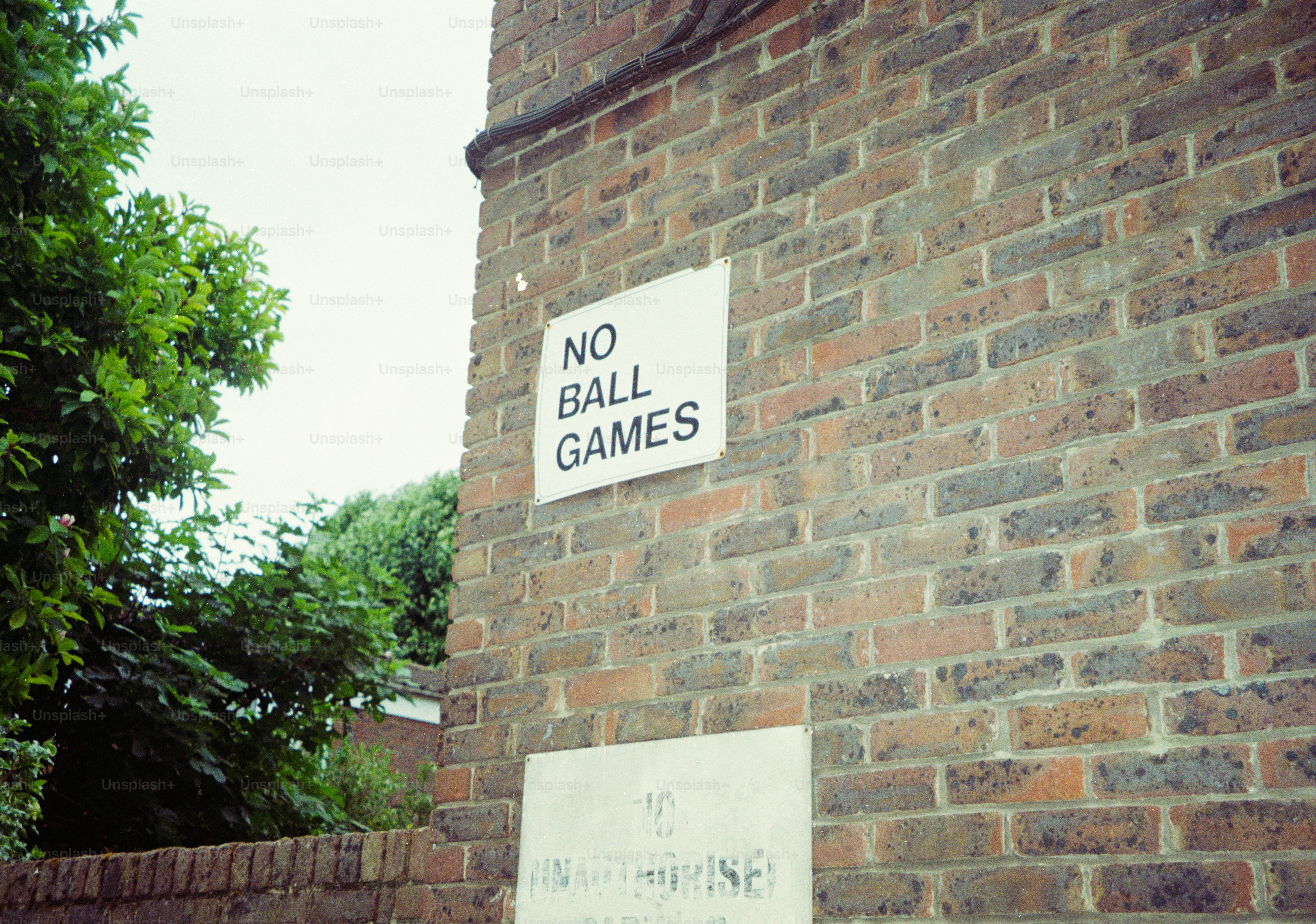 A sign reading "NO BALL GAMES" mounted on a weathered brick wall.