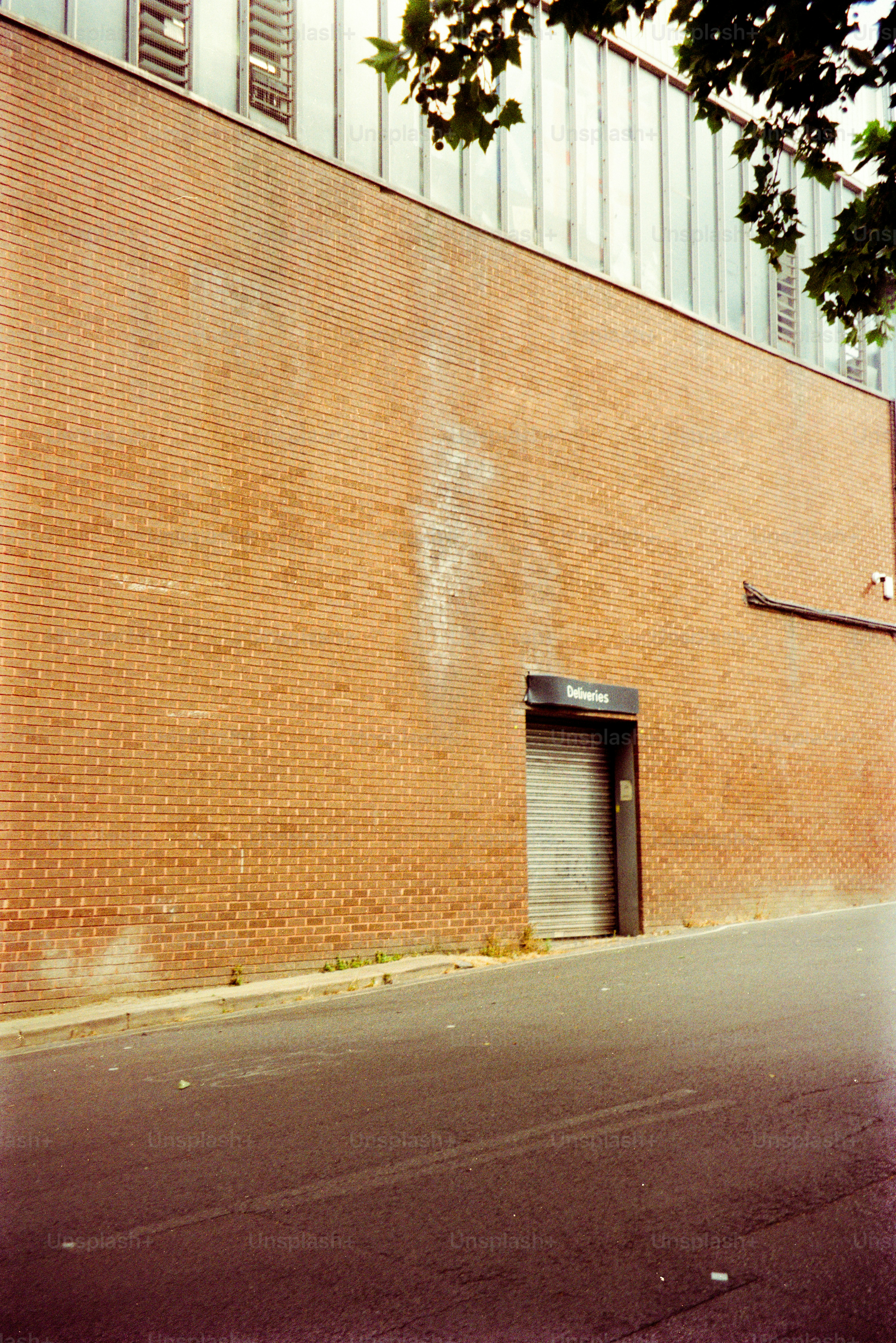 A red brick wall with a metal rolling door labeled "Deliveries" above an asphalt street.