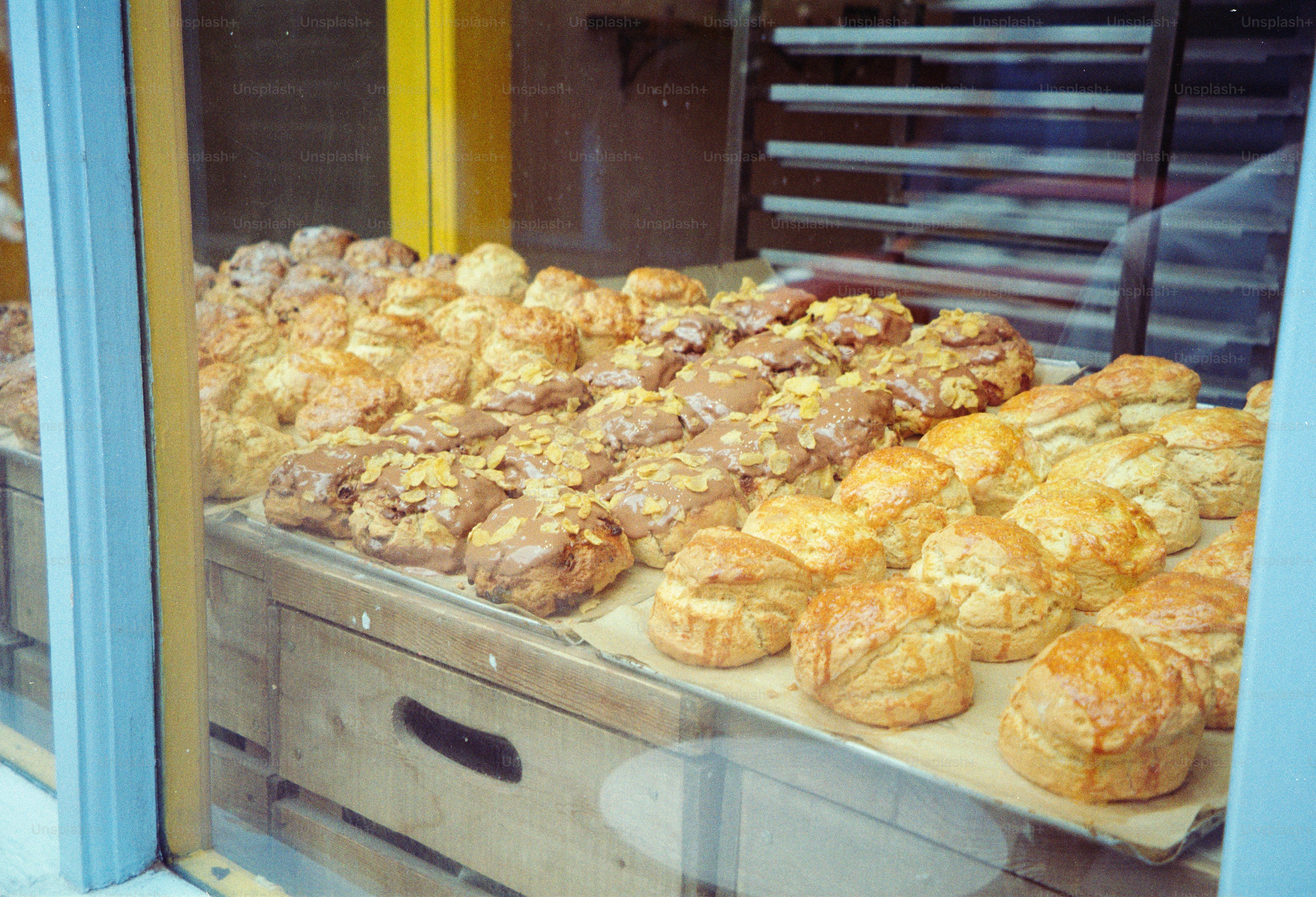 Rows of golden brown scones and glazed pastries in a bakery display window.
