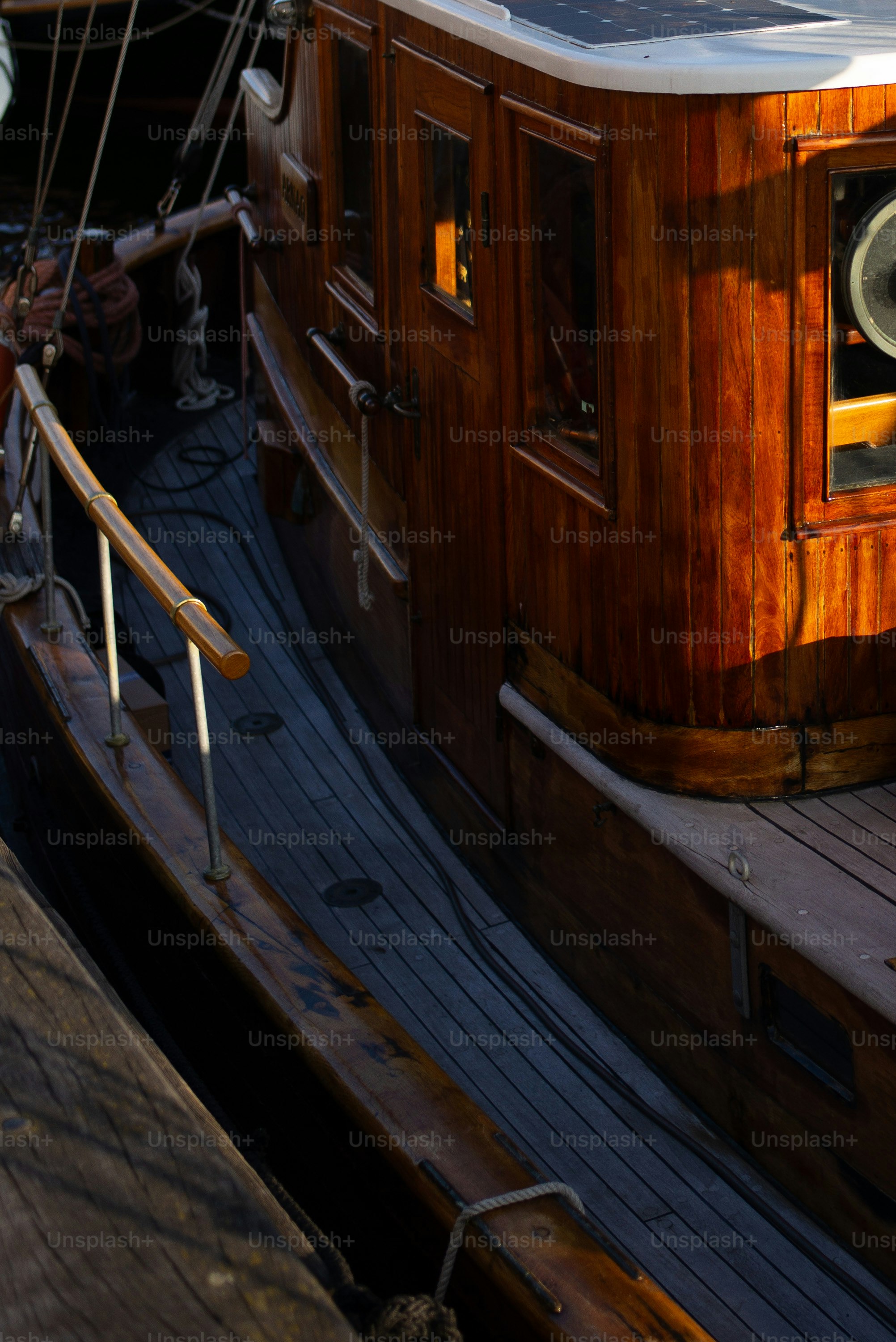 A wooden boat deck with a polished cabin and metal railings in sunlight