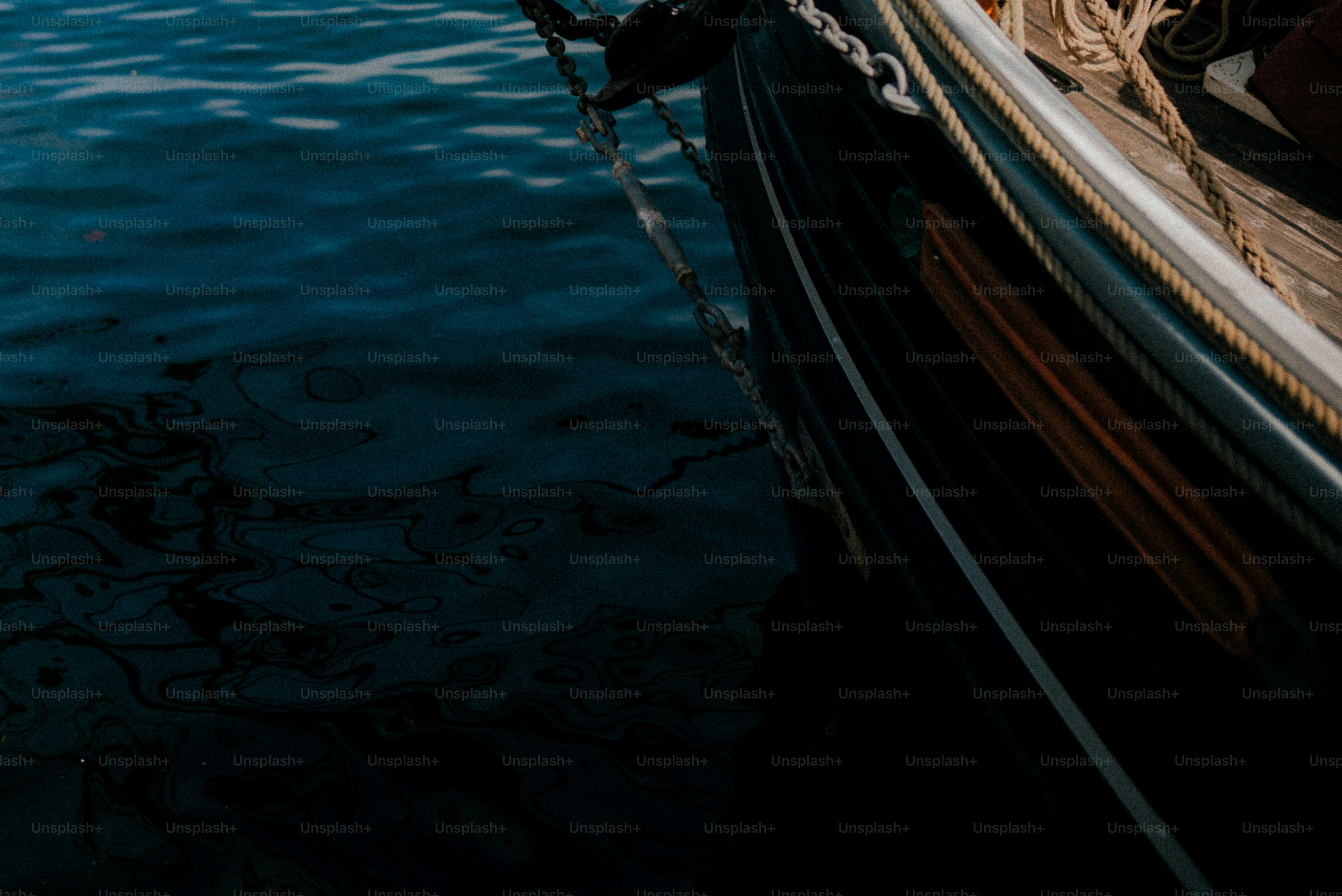 A dark boat hull with a metal chain moored on deep blue water
