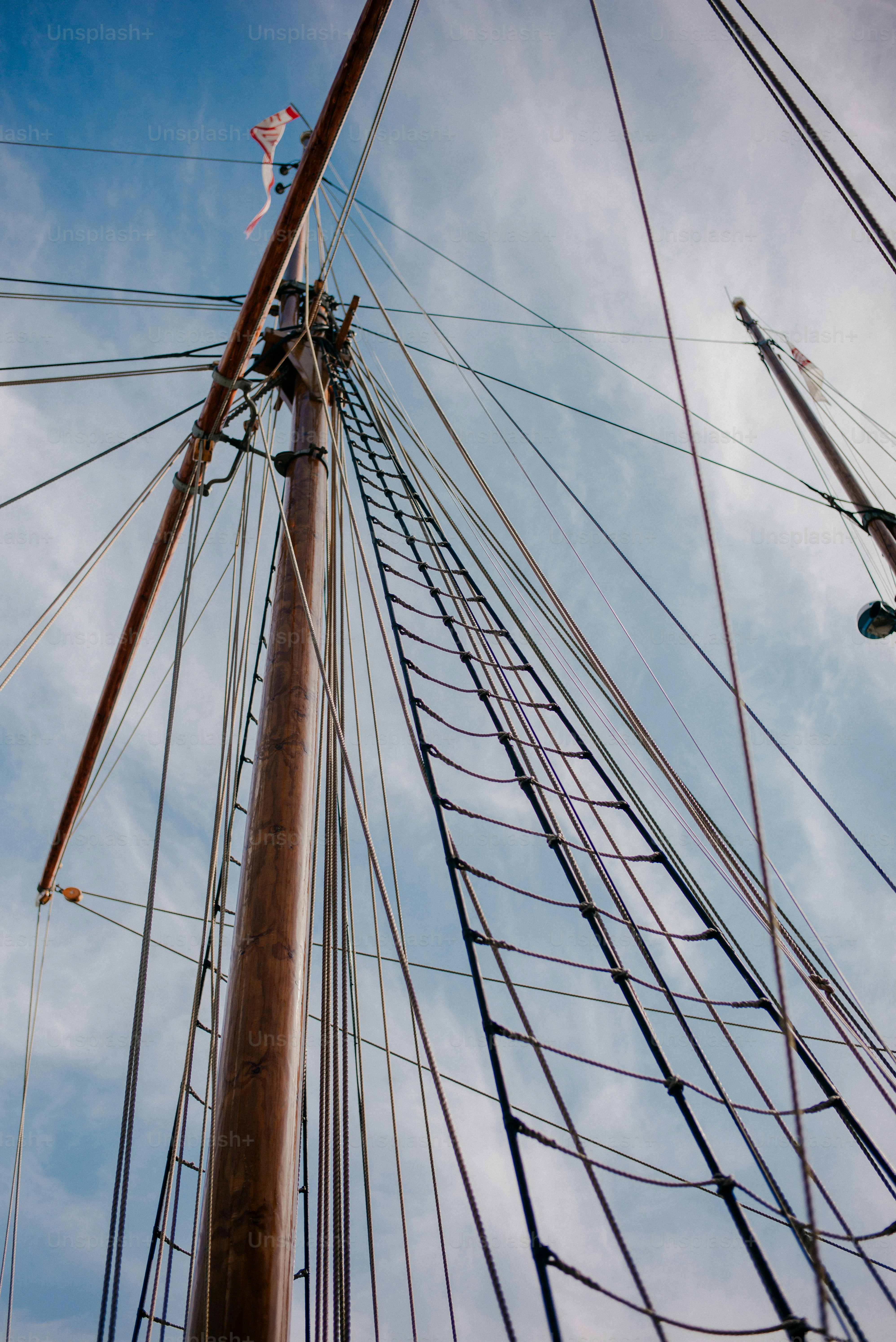 A wooden mast and rope rigging of a sailboat against a cloudy sky