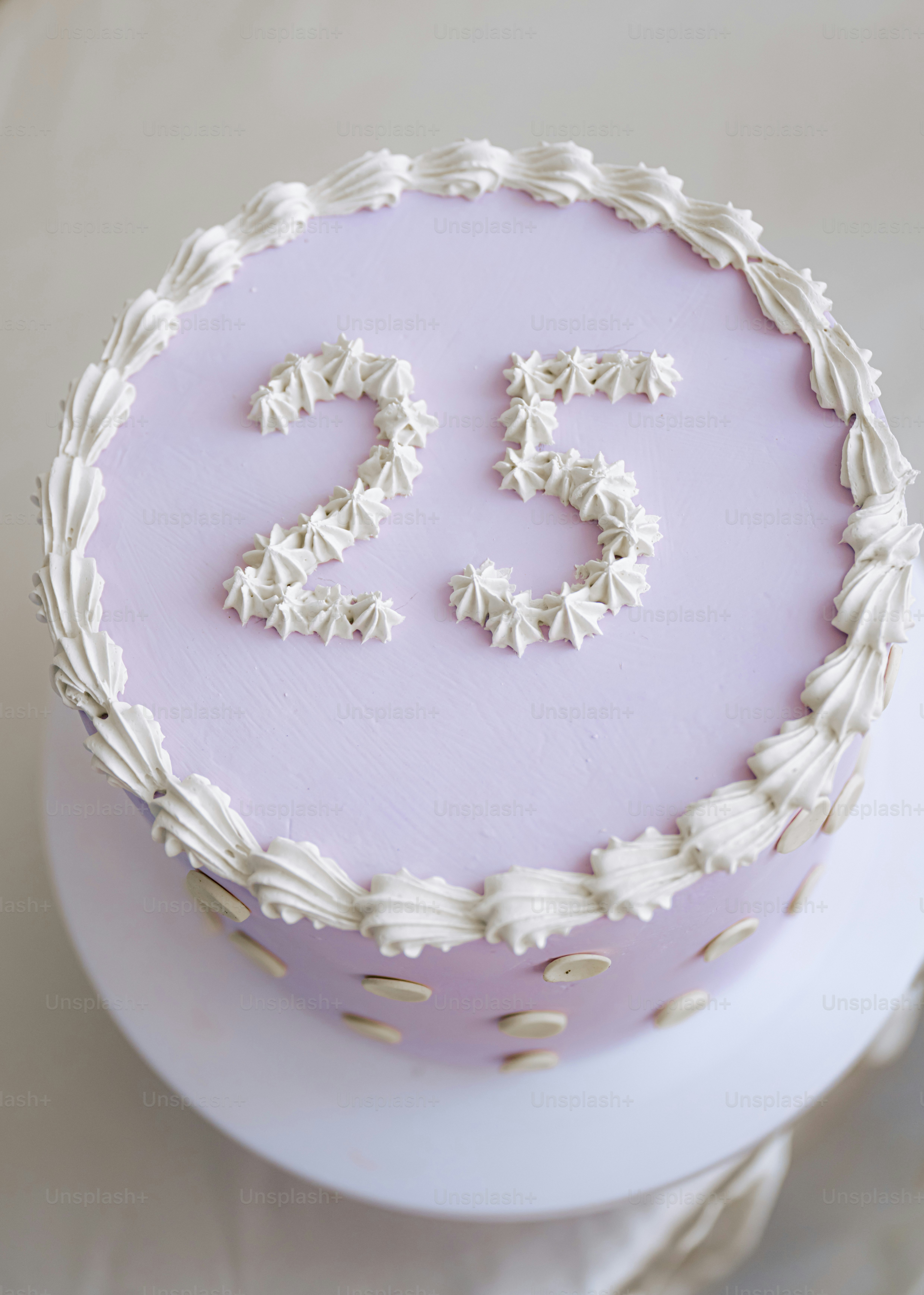 Un pastel redondo con glaseado lila claro y el número veinticinco con pip blanco en la parte superior