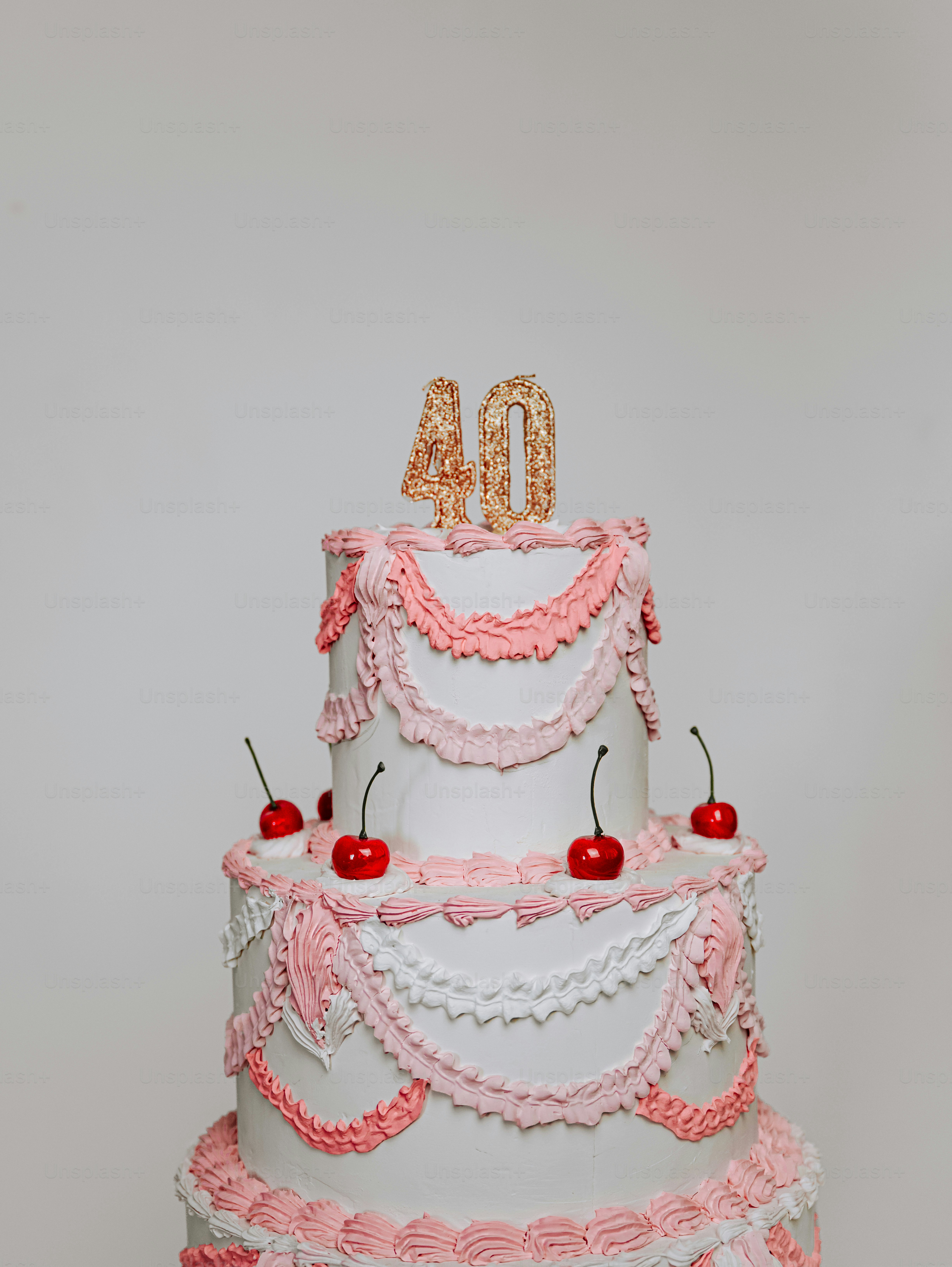 Un pastel blanco de dos niveles con glaseado rosa y cerezas rojas por encima
