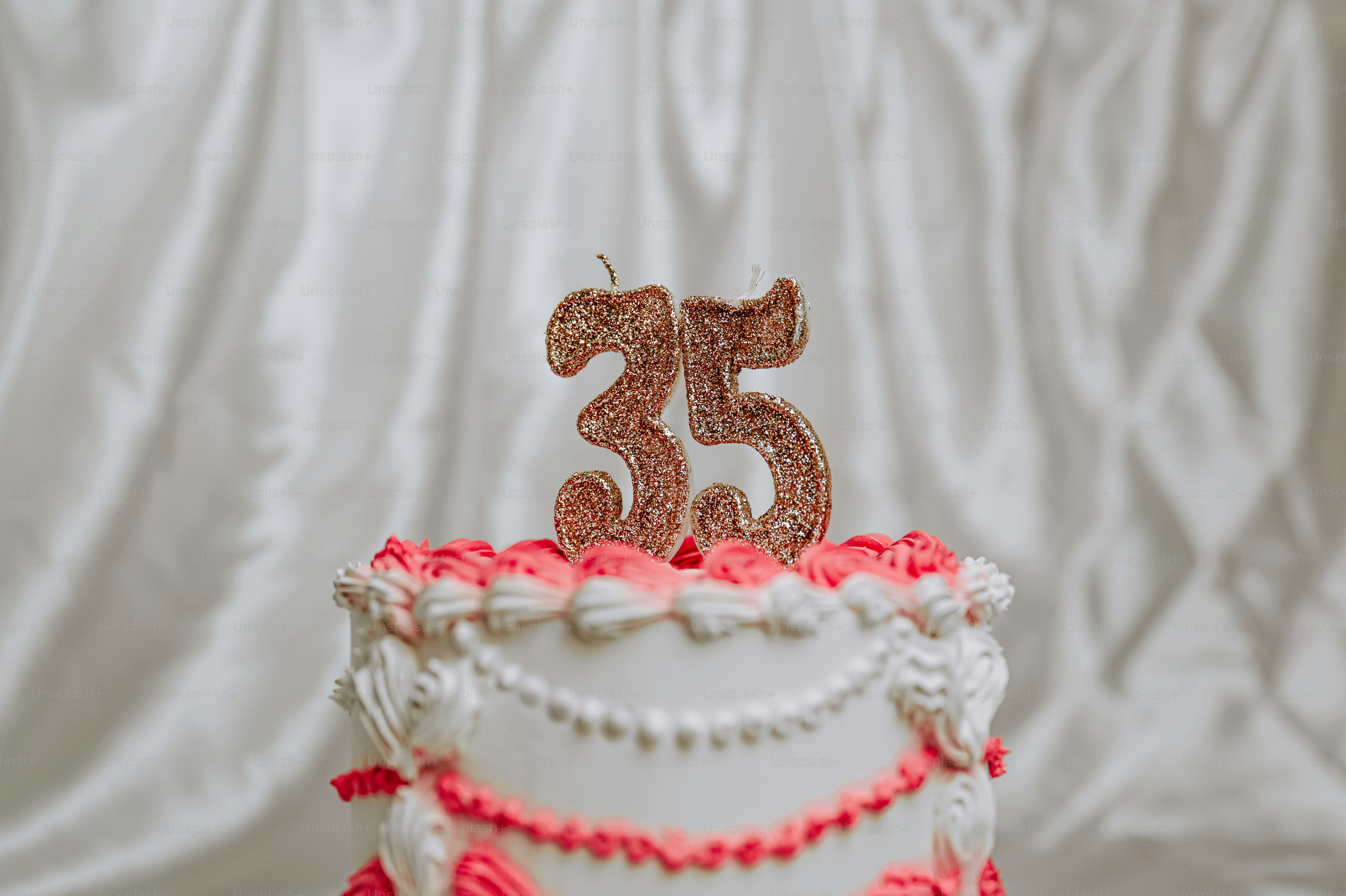 Una tarta blanca con glaseado rosa y velas número treinta y cinco con purpurina