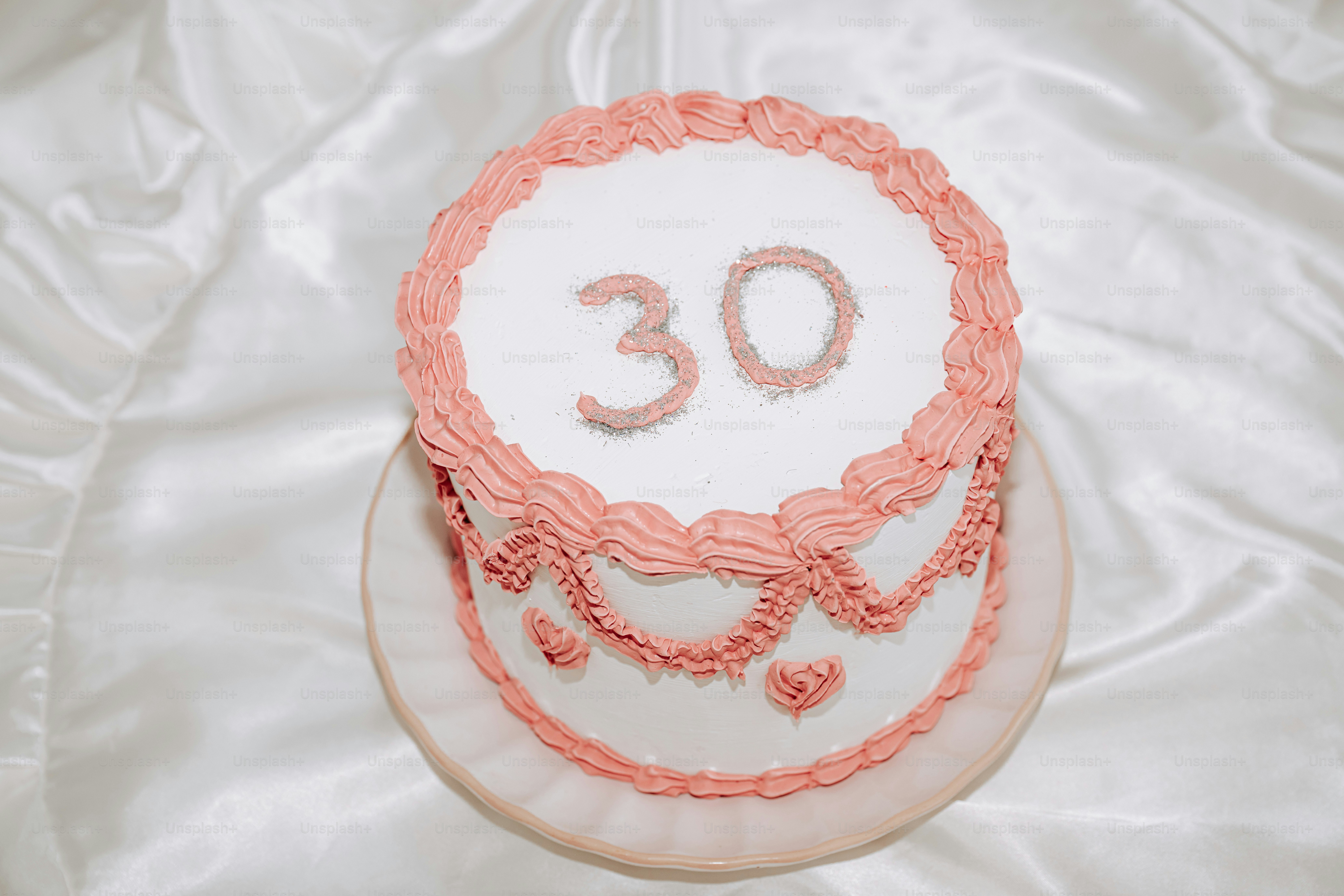 Un pastel blanco con glaseado rosa y el número treinta en un plato