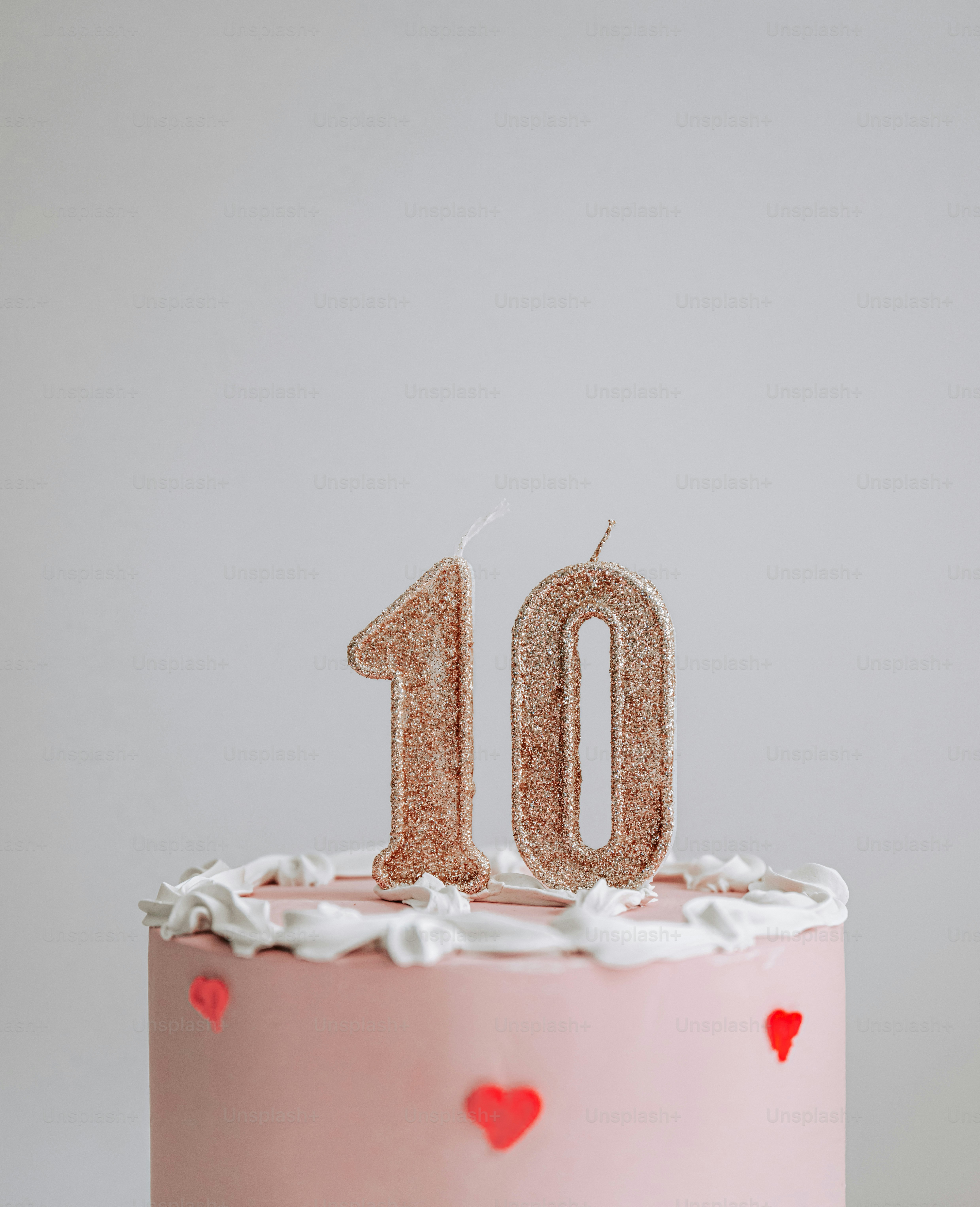 Velas doradas con purpurina número diez sobre un pastel rosa con glaseado blanco y corazones