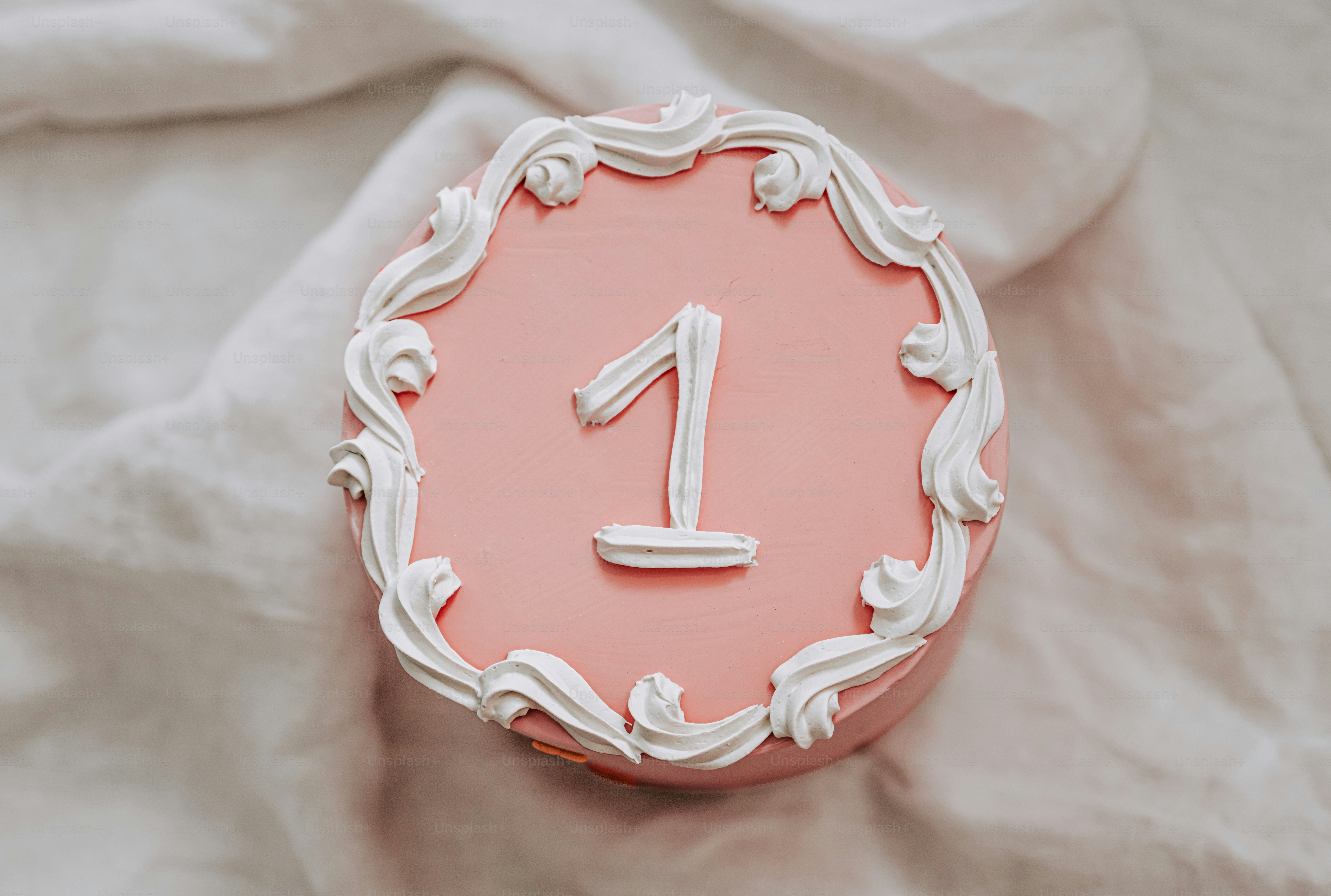 Un pastel rosa con glaseado blanco y el número uno encima