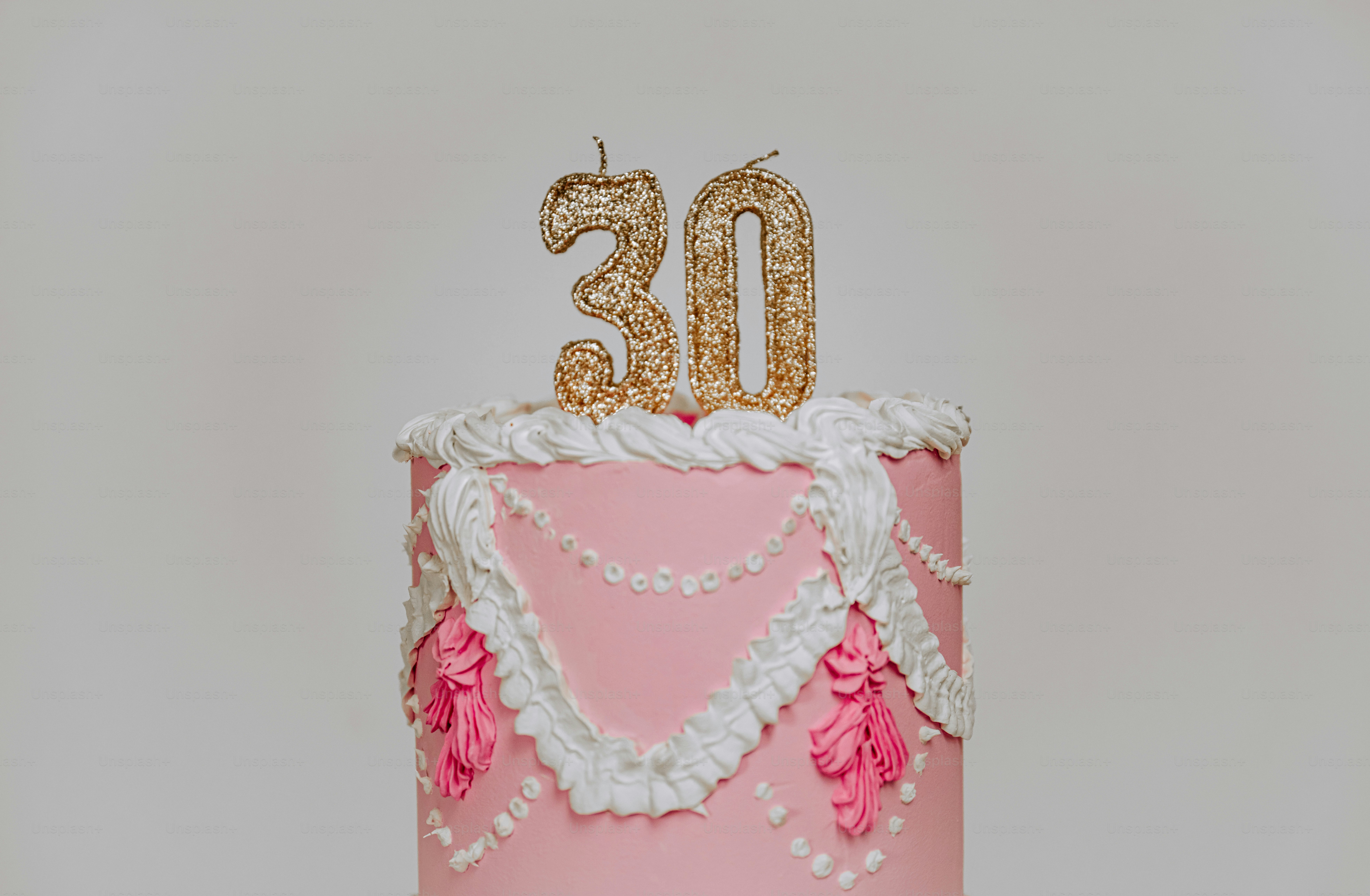 Una tarta de cumpleaños rosa con glaseado blanco y purpurina dorada número treinta velas