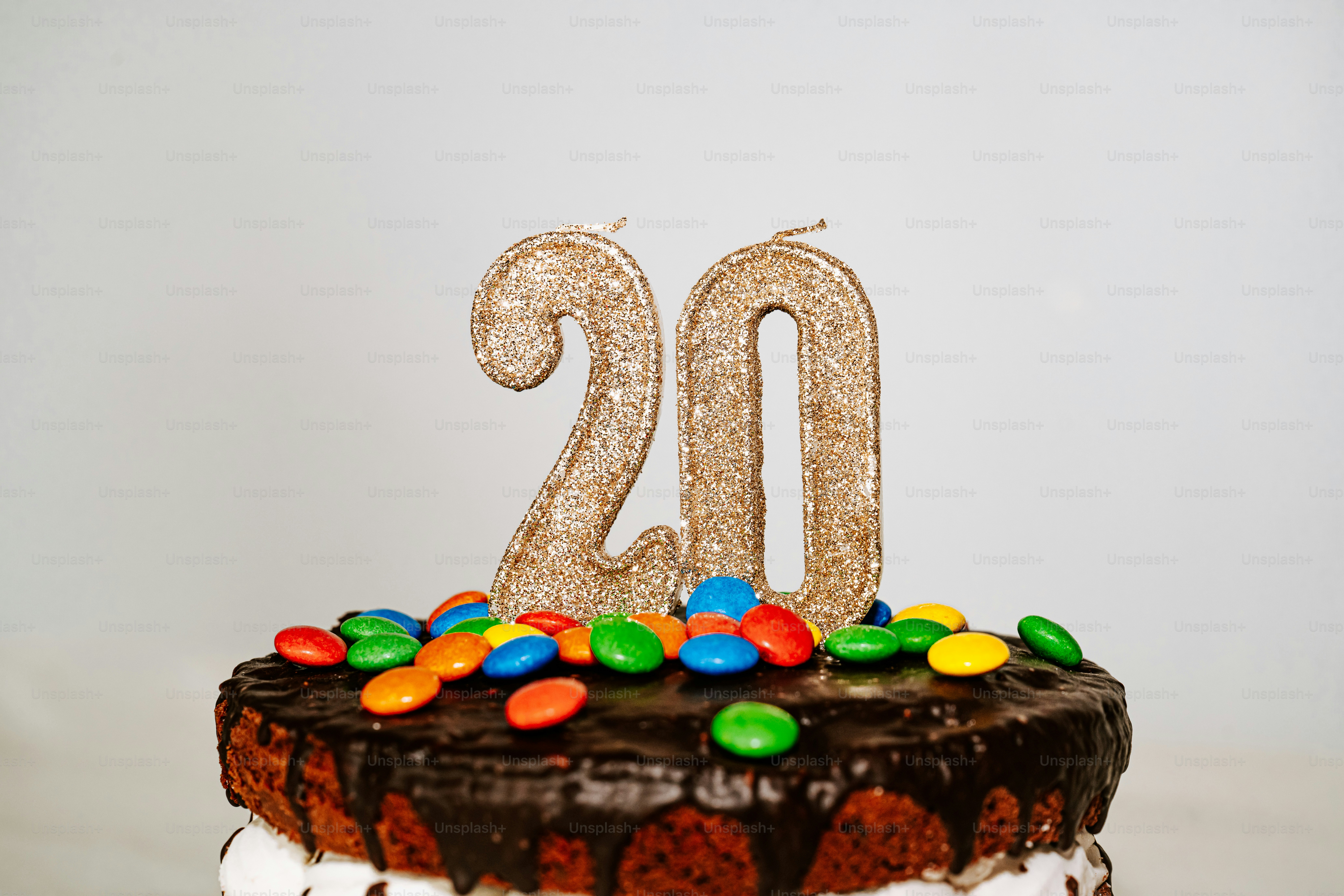 Velas de purpurina dorada número veinte sobre una tarta de chocolate con trozos de caramelos de colores