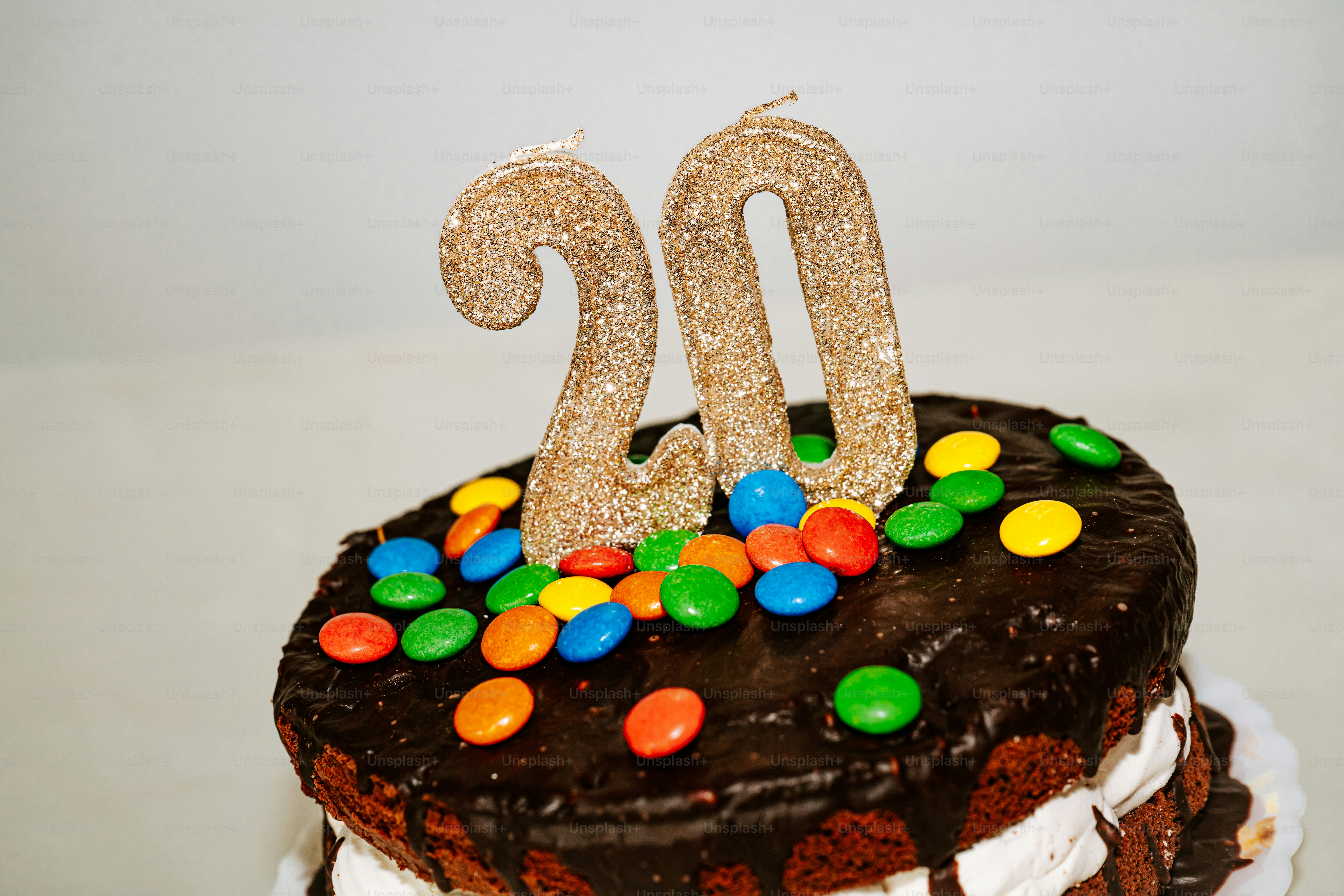 Un pastel de chocolate cubierto con caramelos de colores y velas doradas con purpurina
