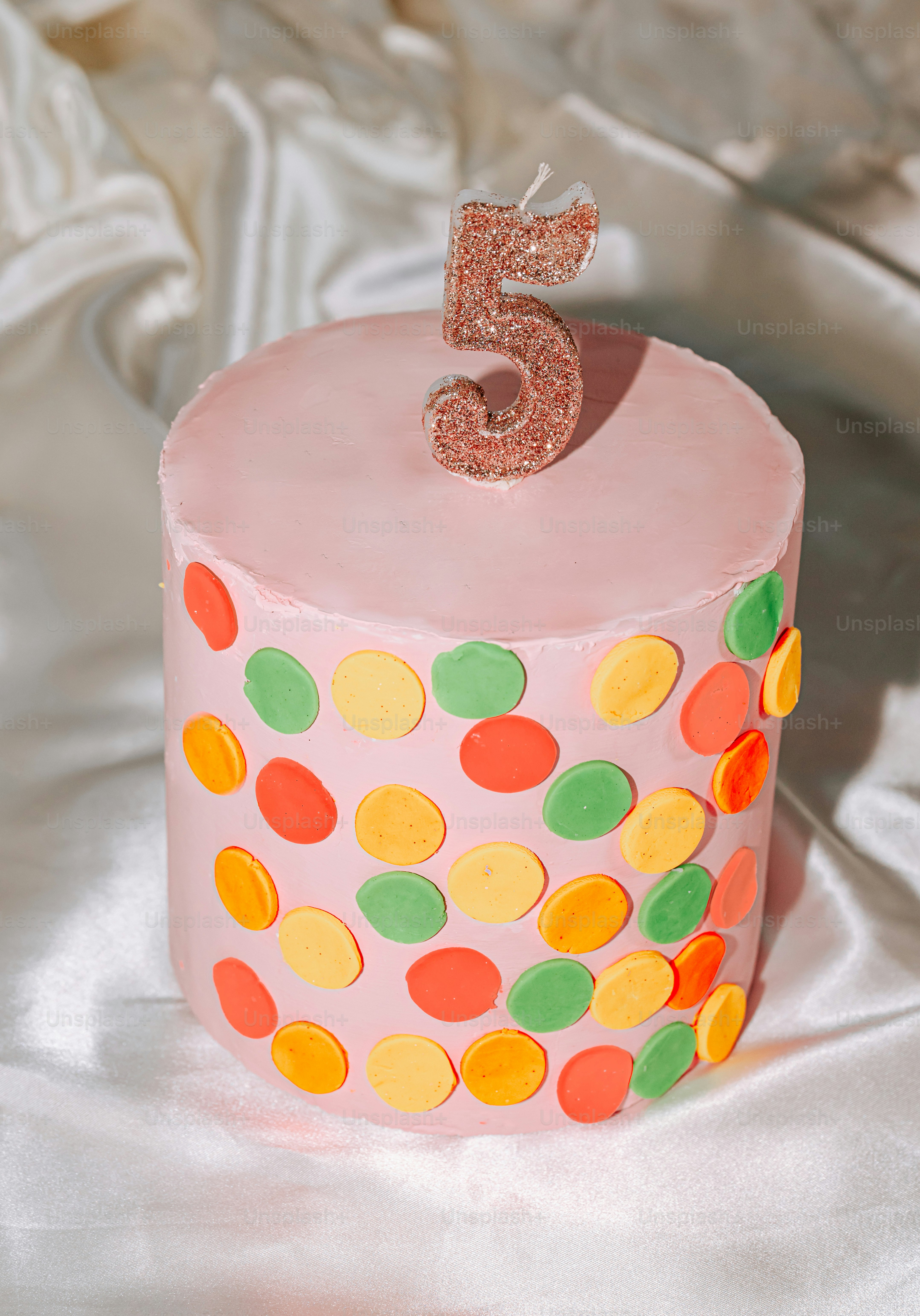 Una tarta rosa decorada con lunares de colores y una vela número cinco brillante