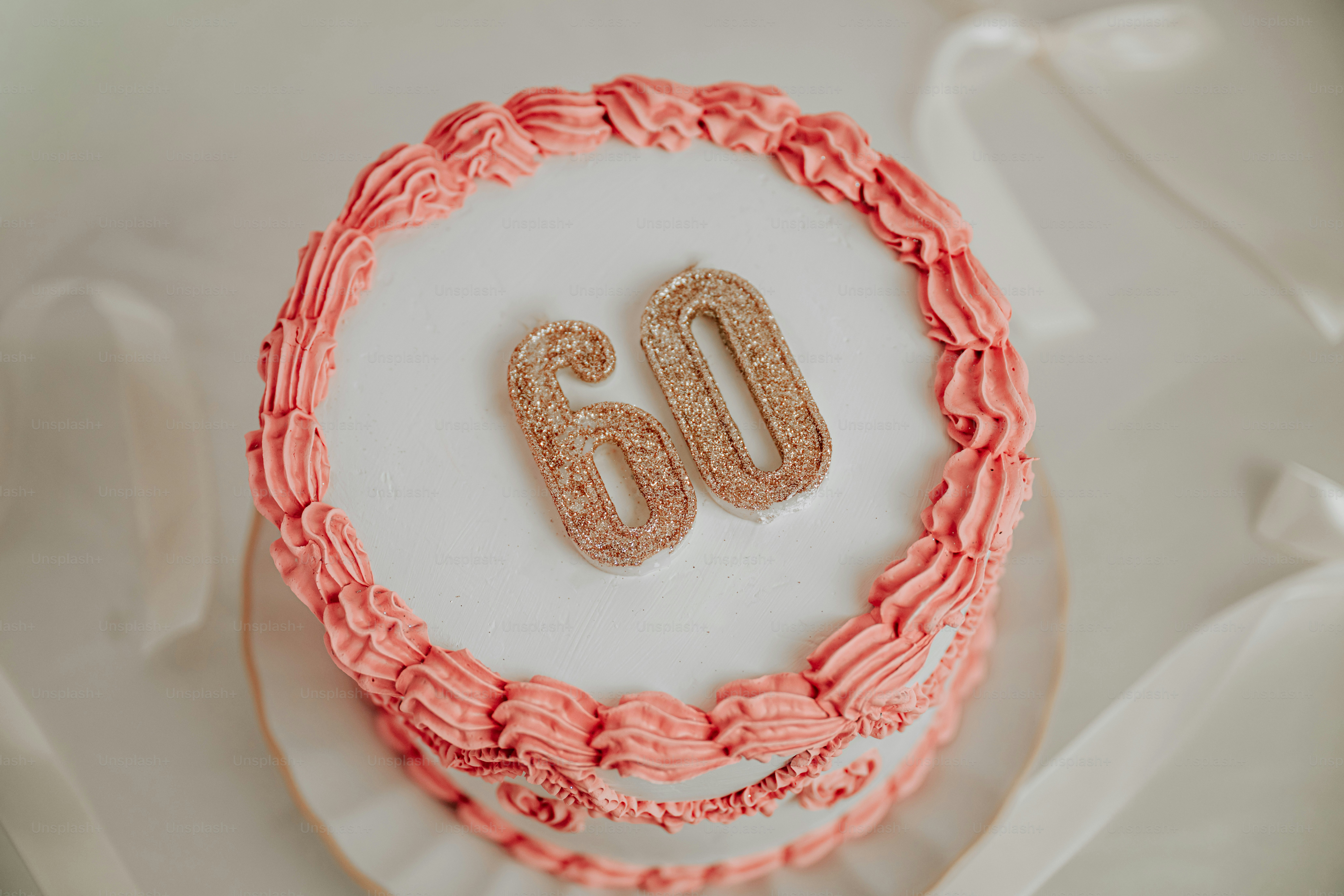 Un pastel blanco con glaseado rosa y velas doradas con purpurina número sesenta