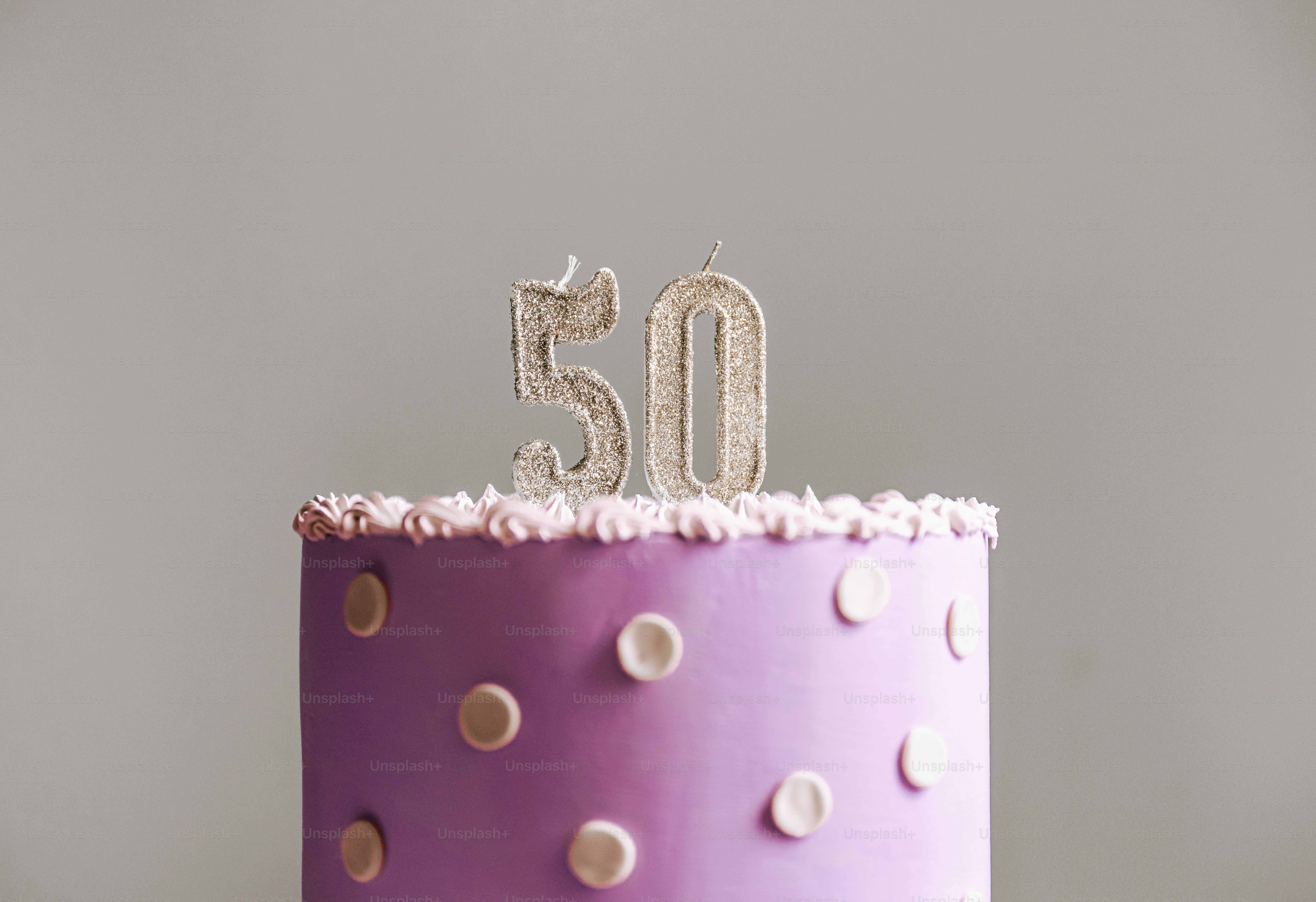 Una tarta morada con lunares blancos y velas número cincuenta con purpurina