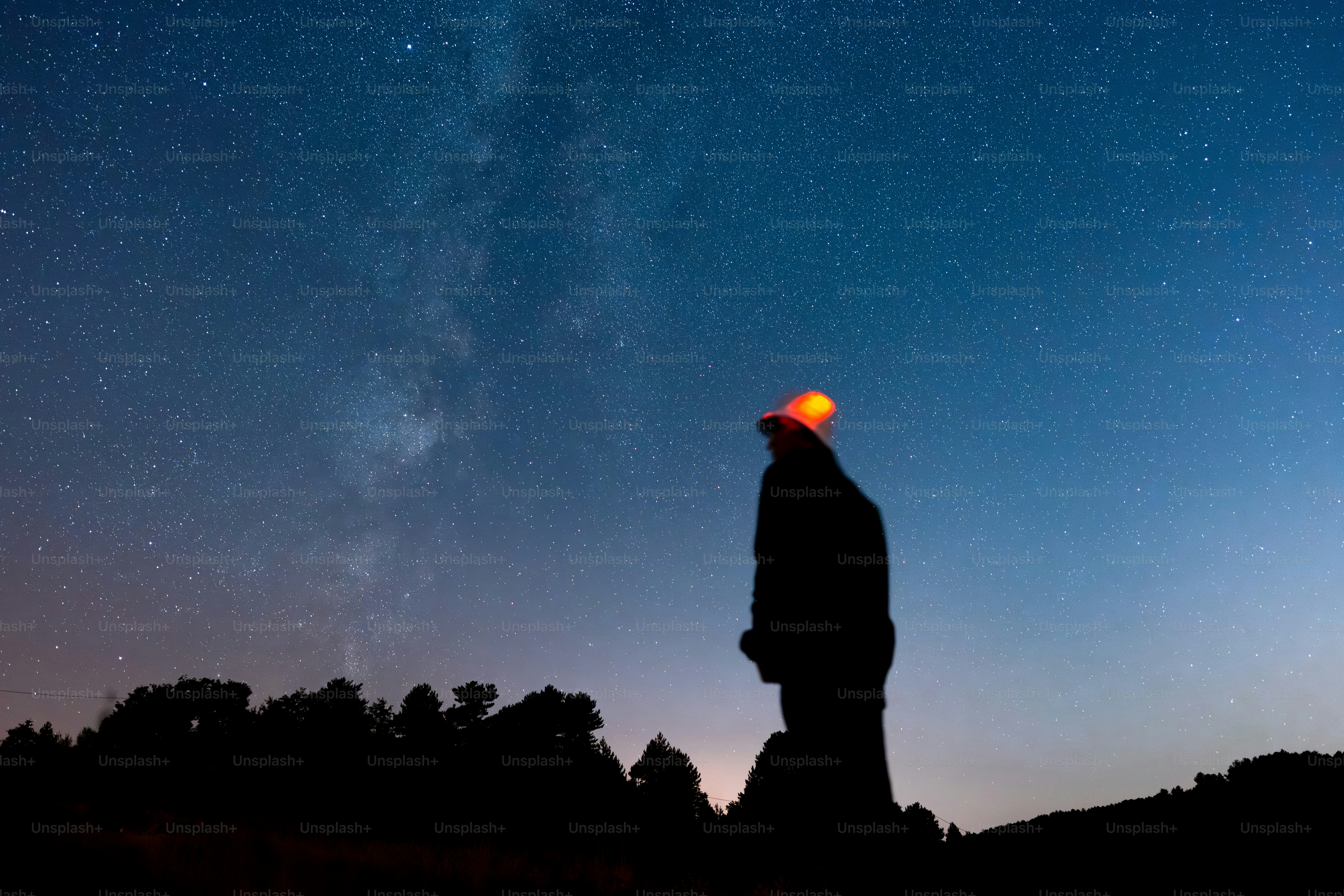 A person in silhouette wearing a glowing orange hat under a starry night sky
