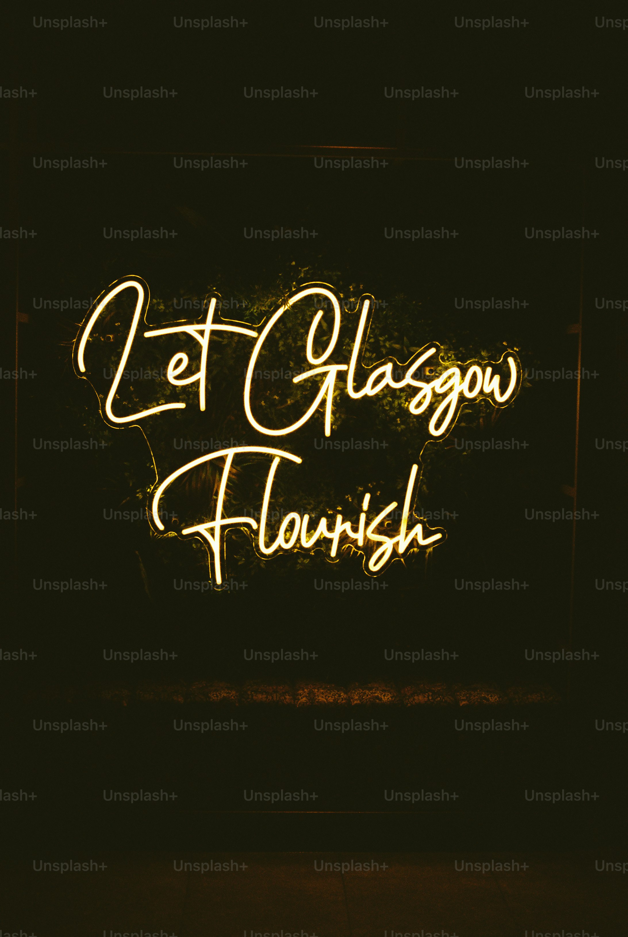 A glowing yellow neon sign reading Let Glasgow Flourish against a dark background