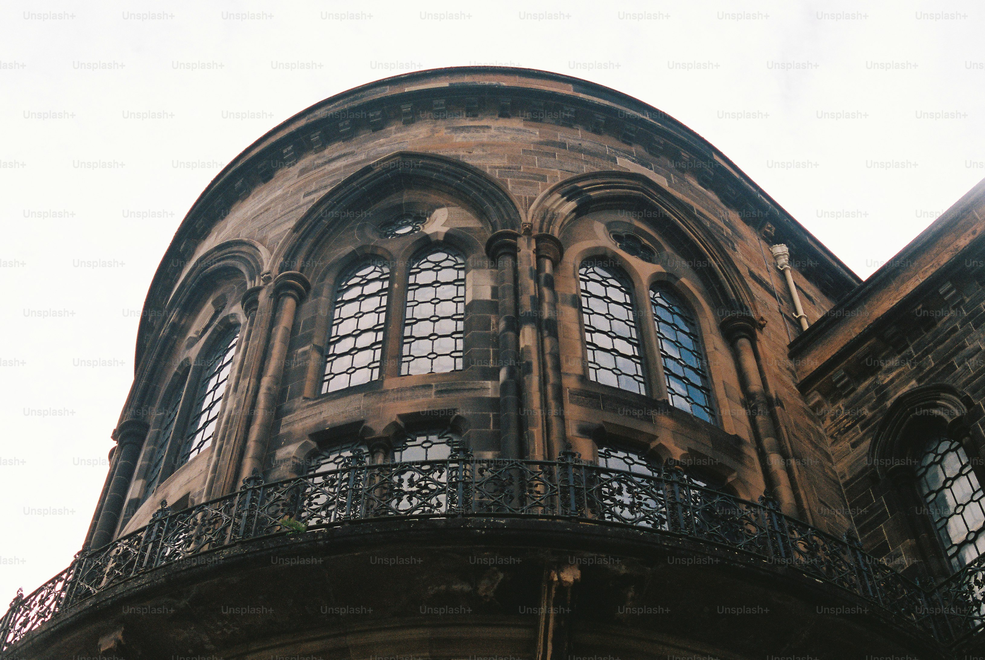 A curved stone building with gothic arched windows and a decorative iron balcony