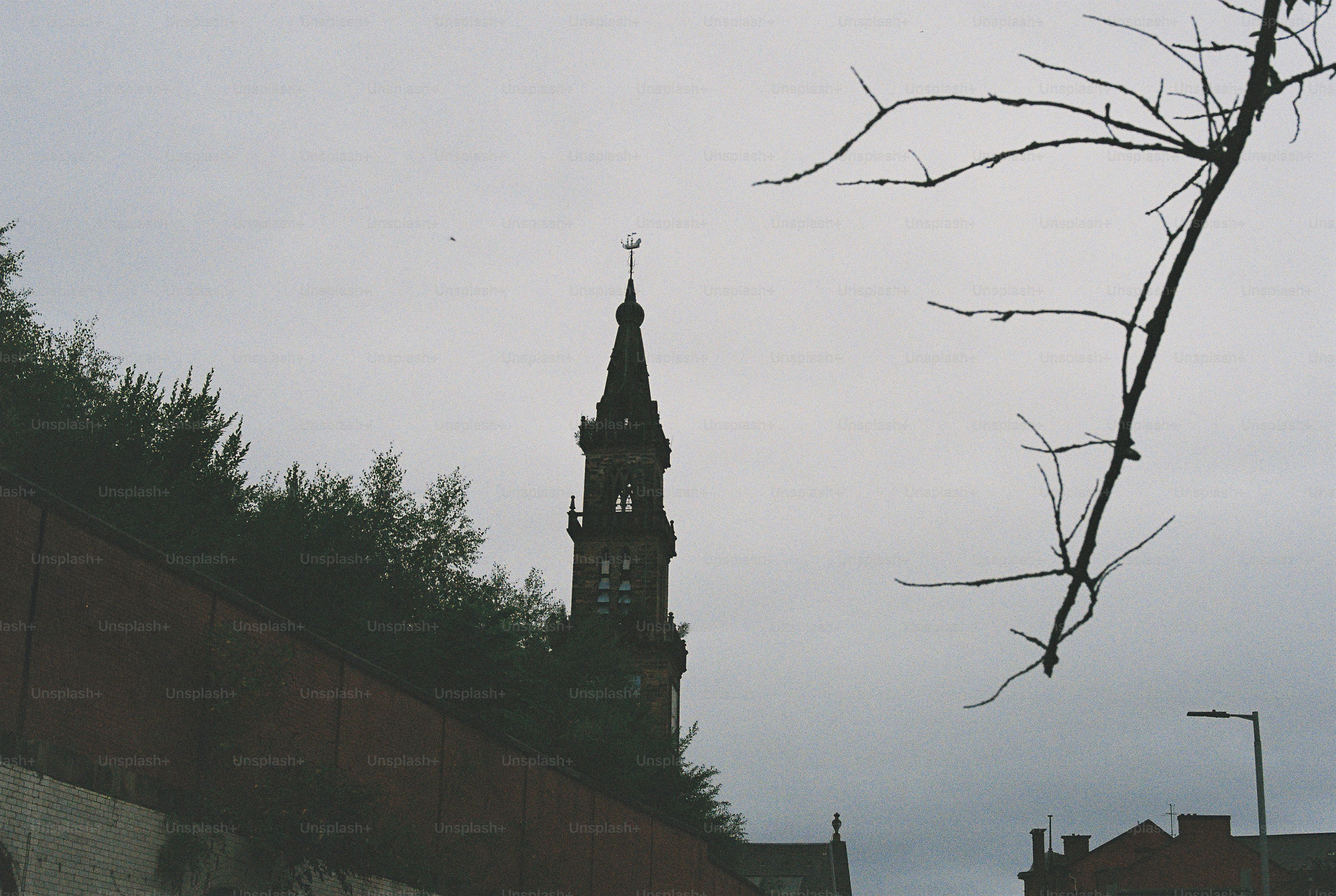 A stone church tower rising above a brick wall under a grey sky