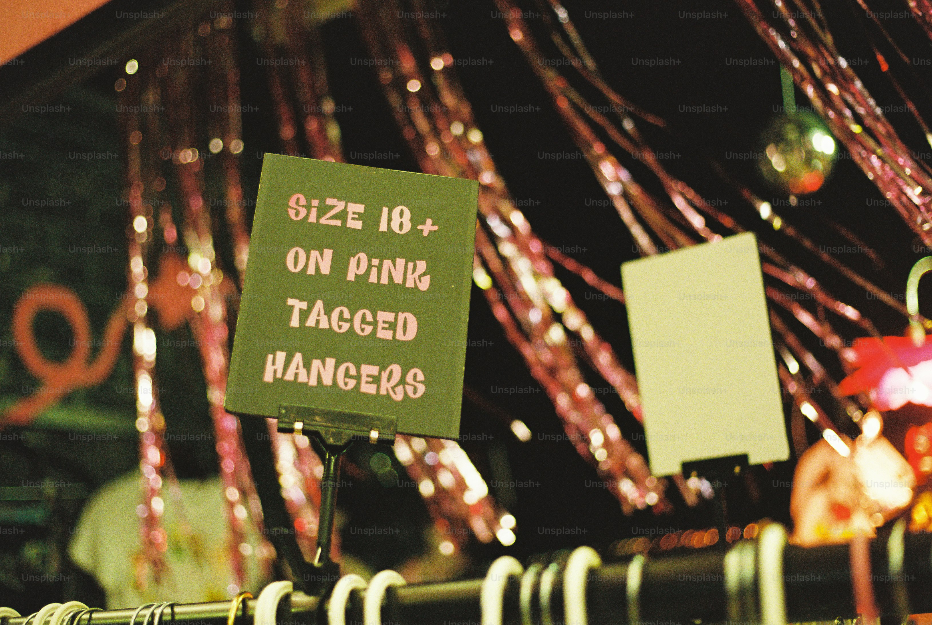 A sign reading "SIZE 18+ ON PINK TAGGED HANGERS" with pink tinsel in background