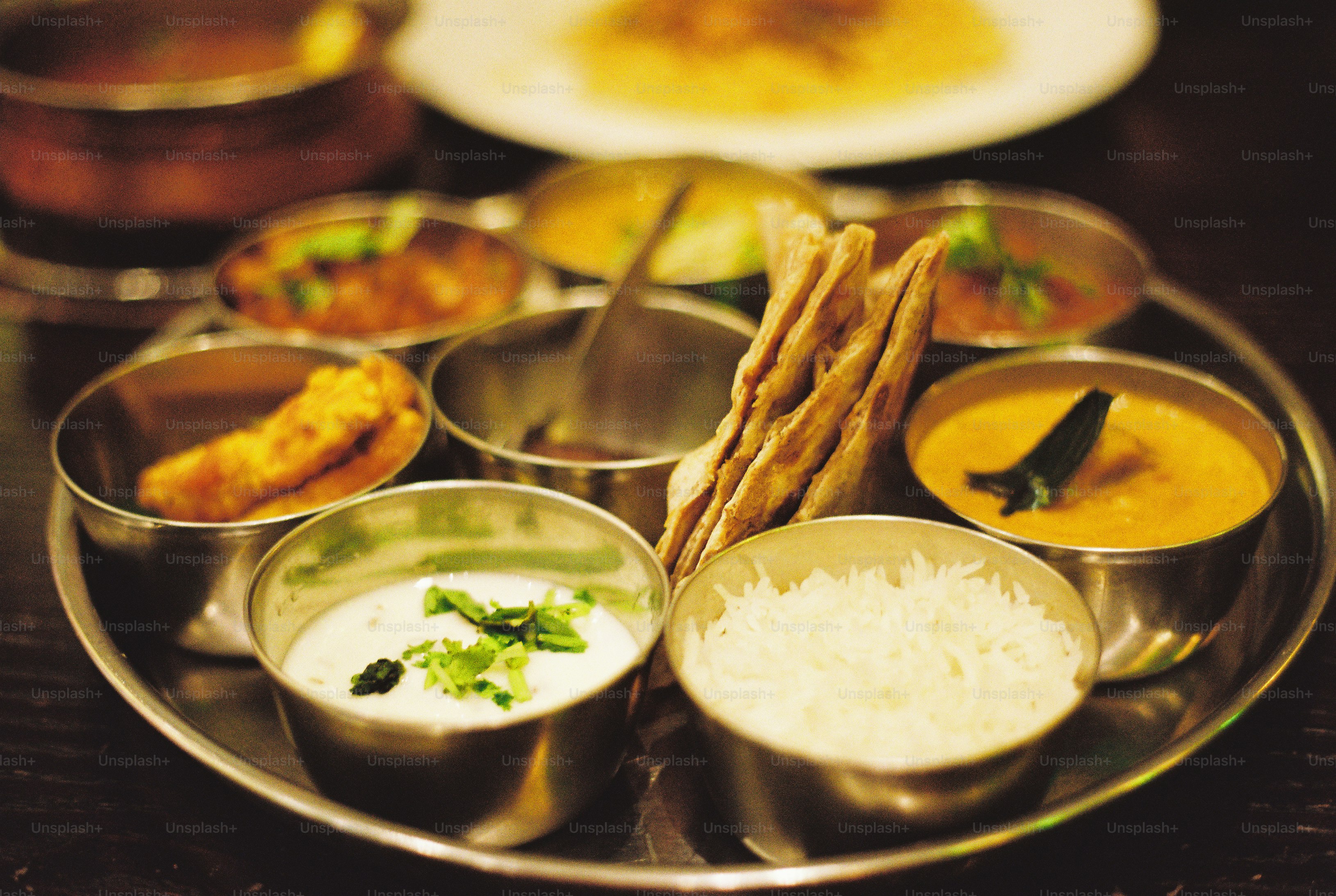 A metal thali platter with small bowls of curry, rice, yogurt, and flatbread