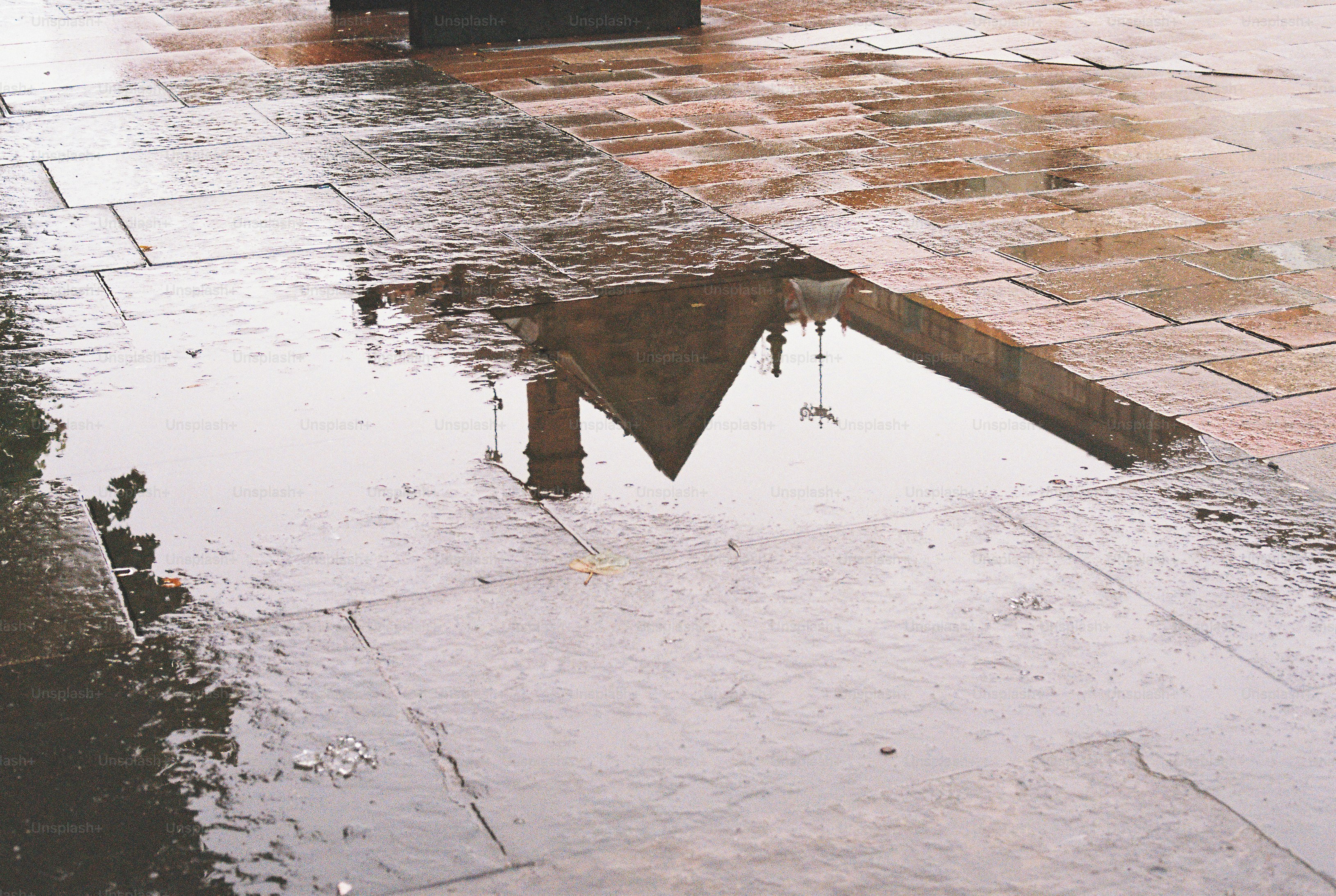 A reflection of a building in a large puddle on wet stone pavers