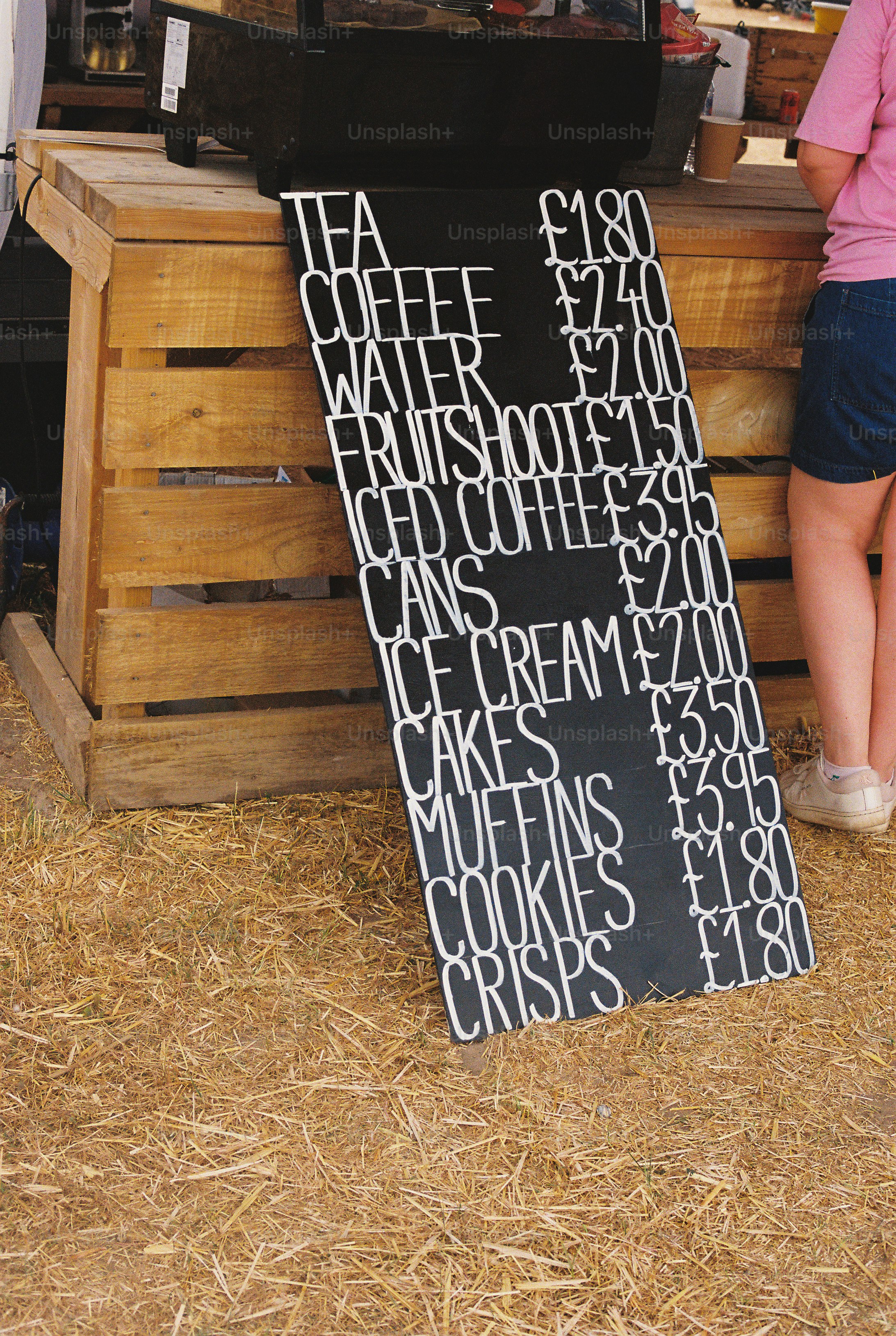 A chalkboard menu with prices leaning against a wooden stall on straw ground