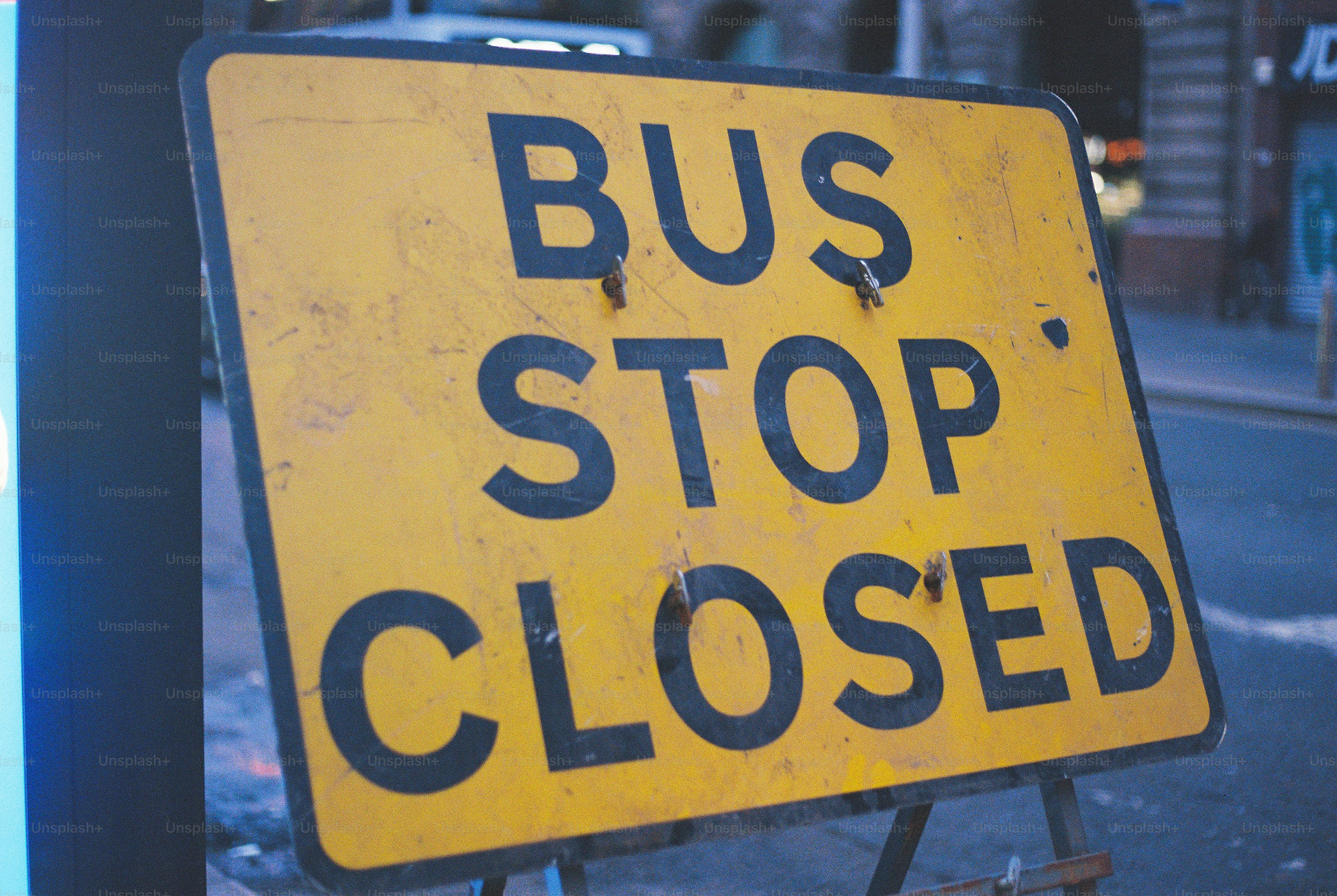 A yellow sign with black text reading BUS STOP CLOSED on a street