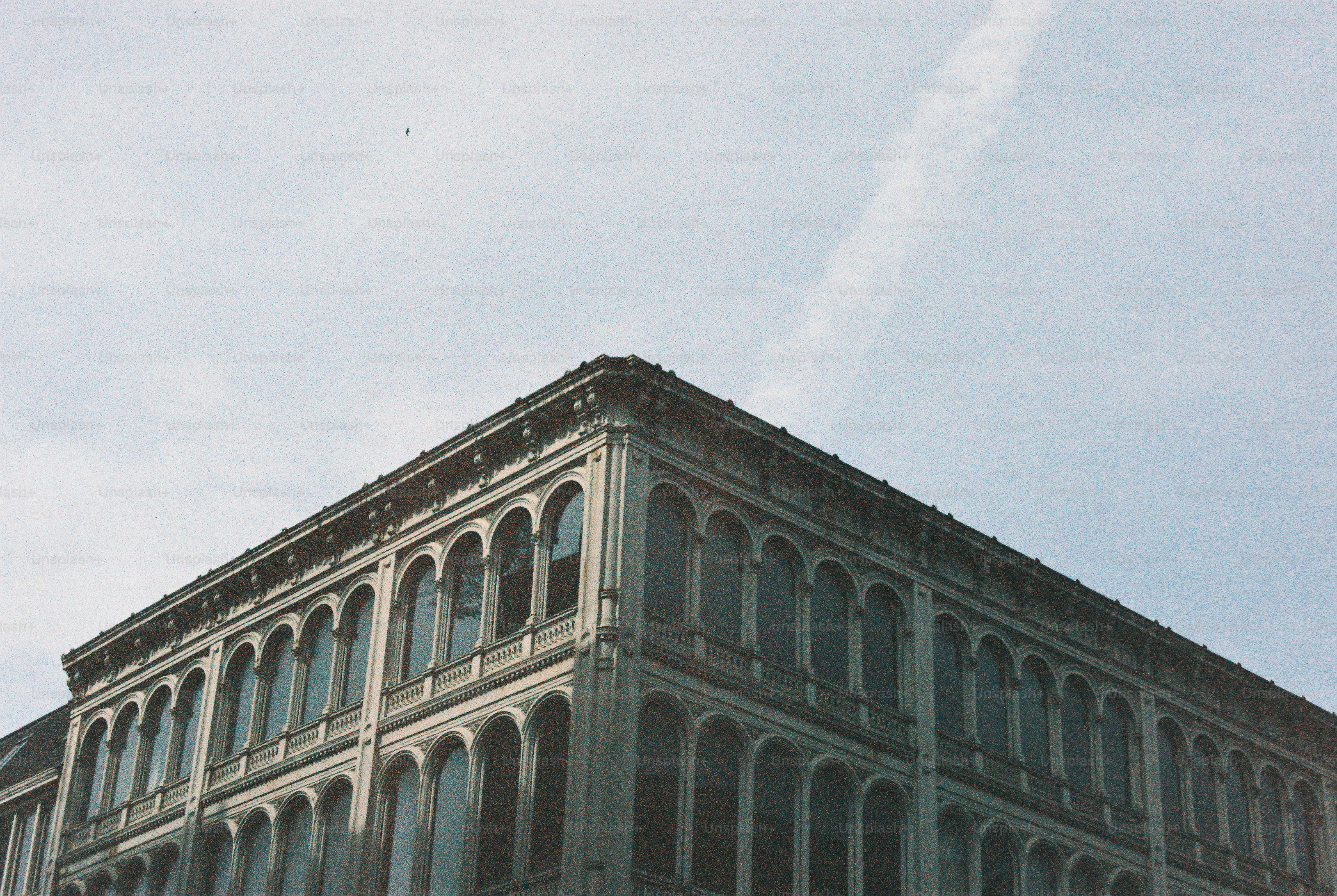 A corner view of a building with arched windows against a pale sky