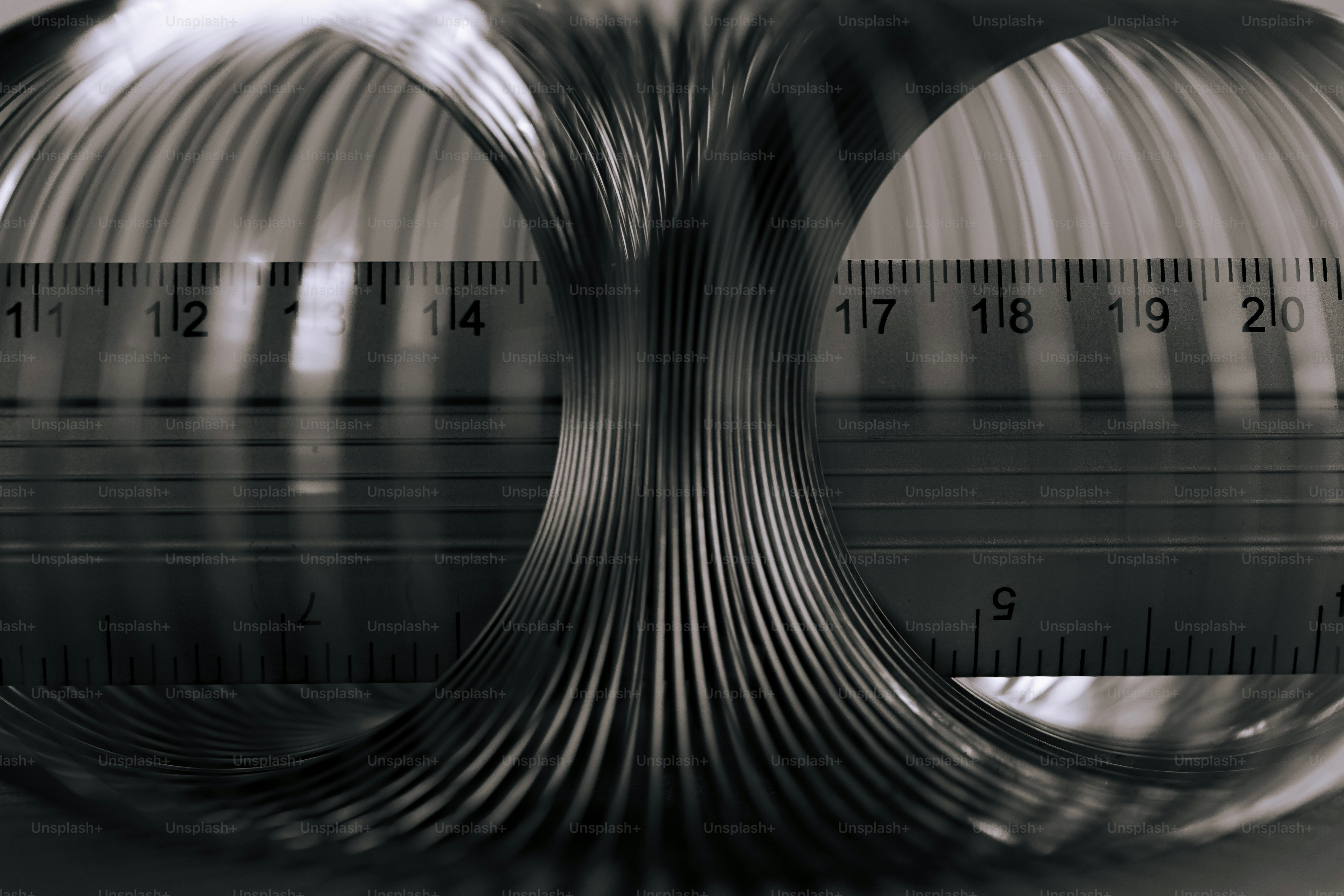 Ein metallisches Slinky-Spielzeug, das sich um ein Lineal mit sichtbaren Maßmarkierungen windete, gewickelt