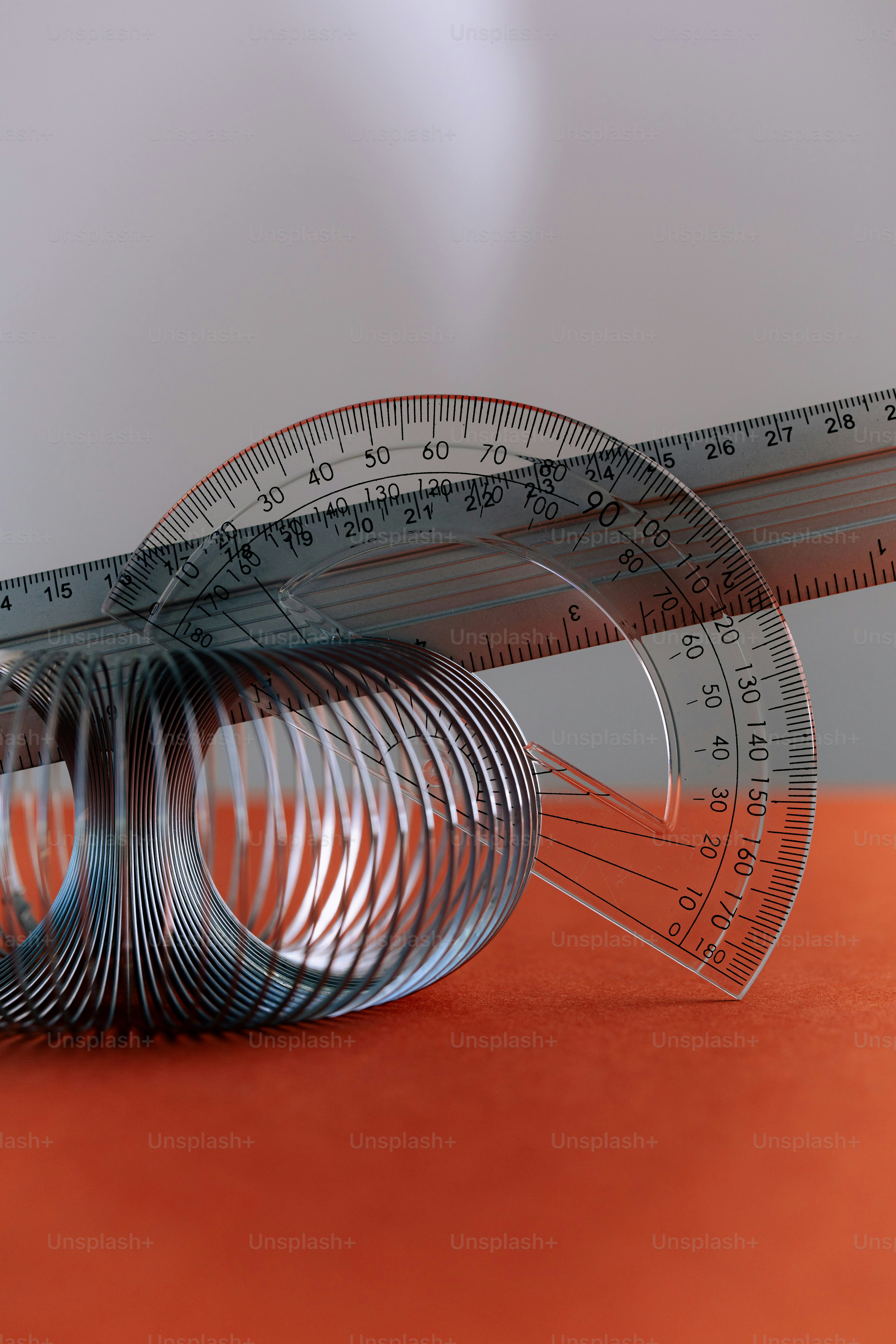 A metal slinky, a clear plastic protractor, and a ruler on an orange surface