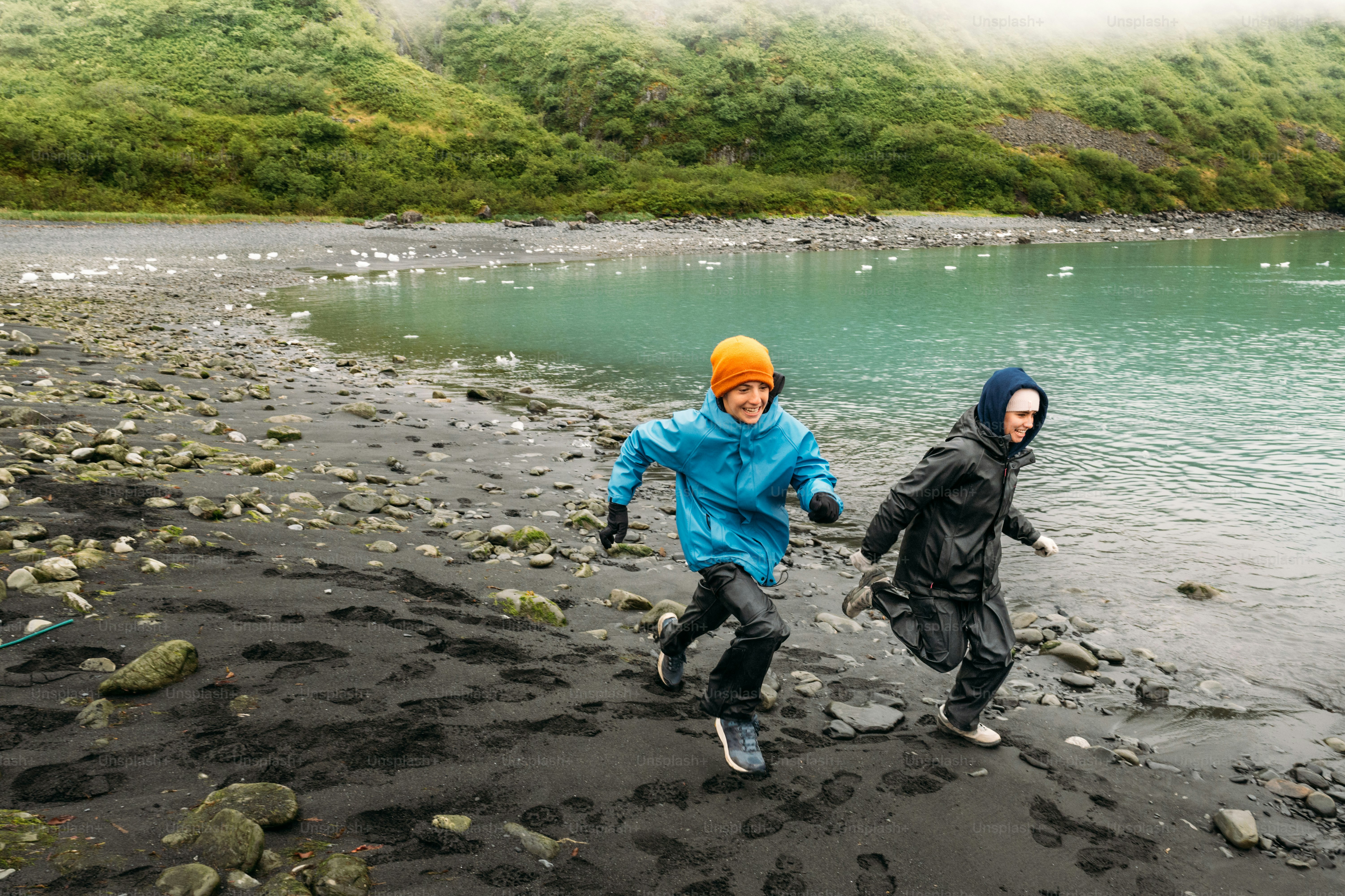 Hermanos con impermeables corren en la playa de la bahía glaciar en Alaska