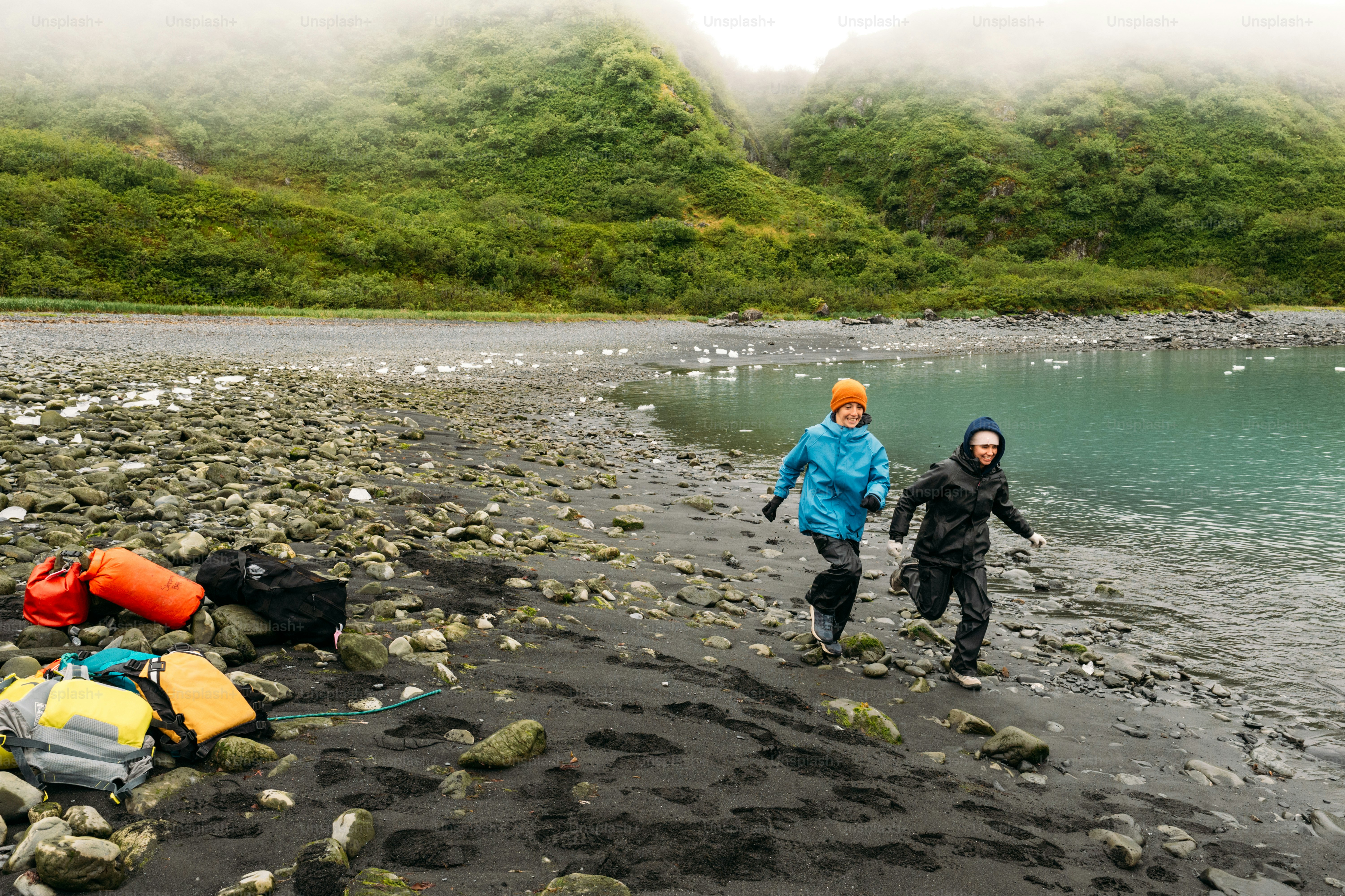 Hermanos con impermeables corren en la playa de la bahía glaciar en Alaska