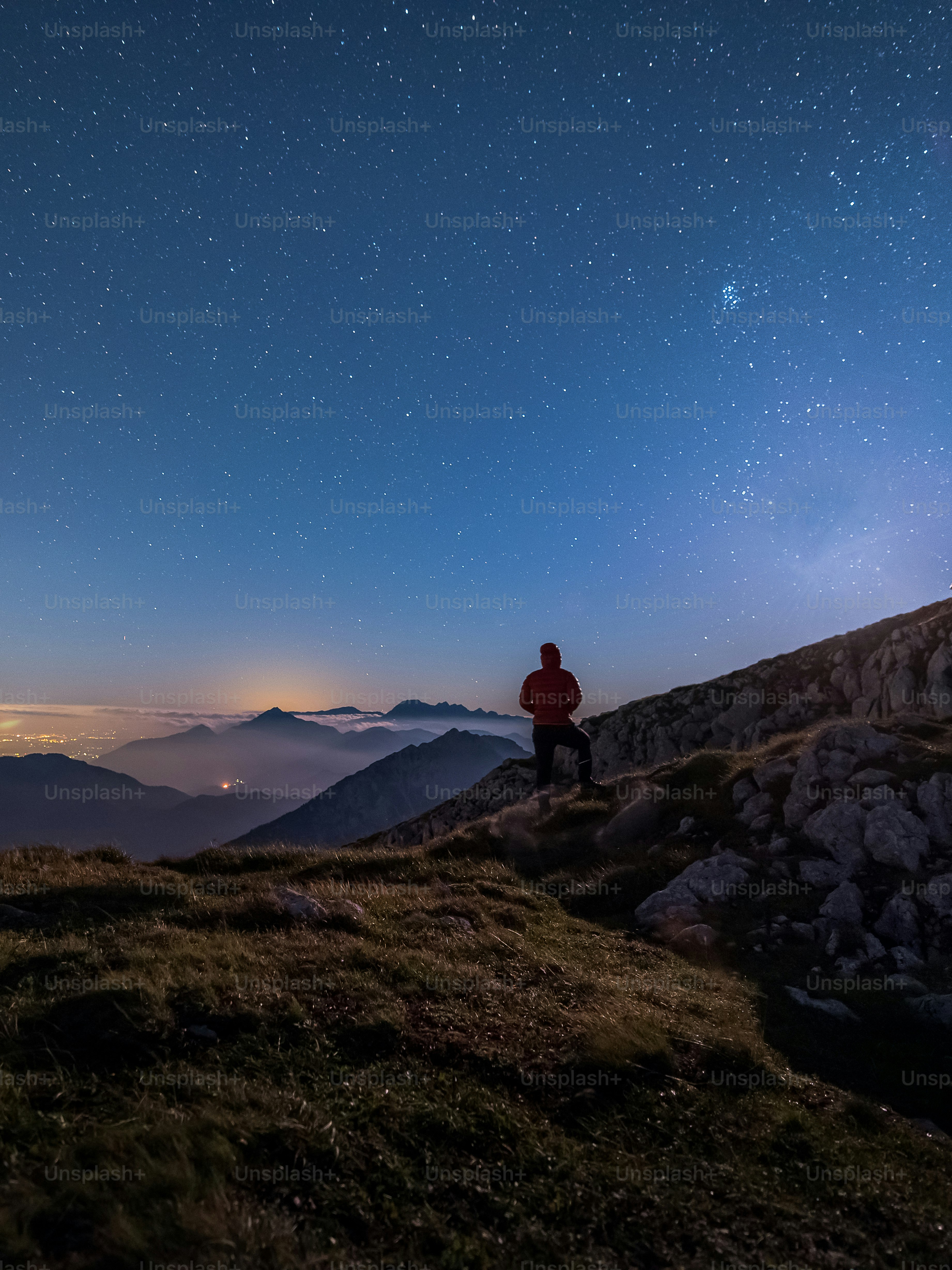 A person in a red jacket on a rocky mountain ridge under starry skies