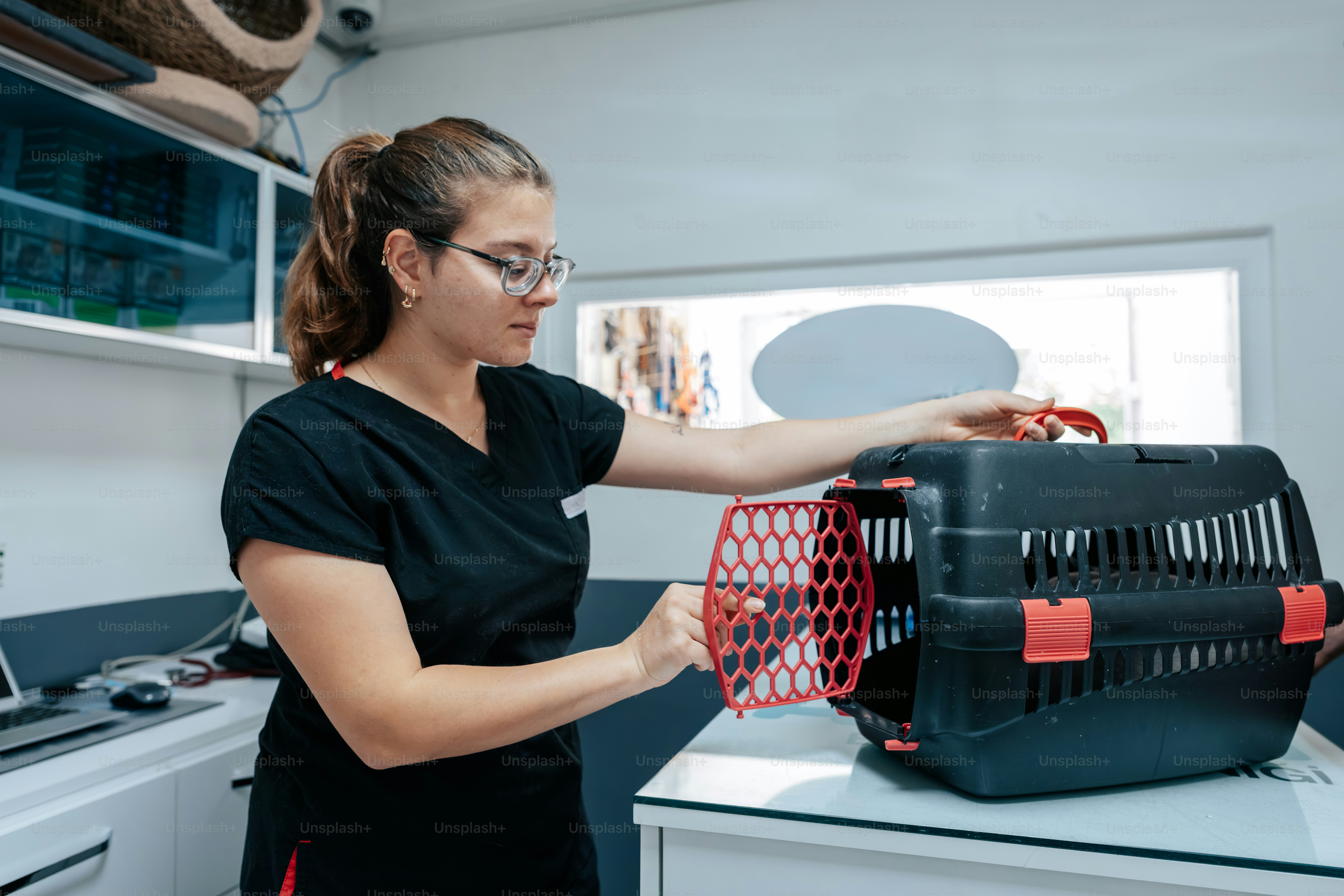 A woman in black scrubs opening a black pet carrier on a clinic table