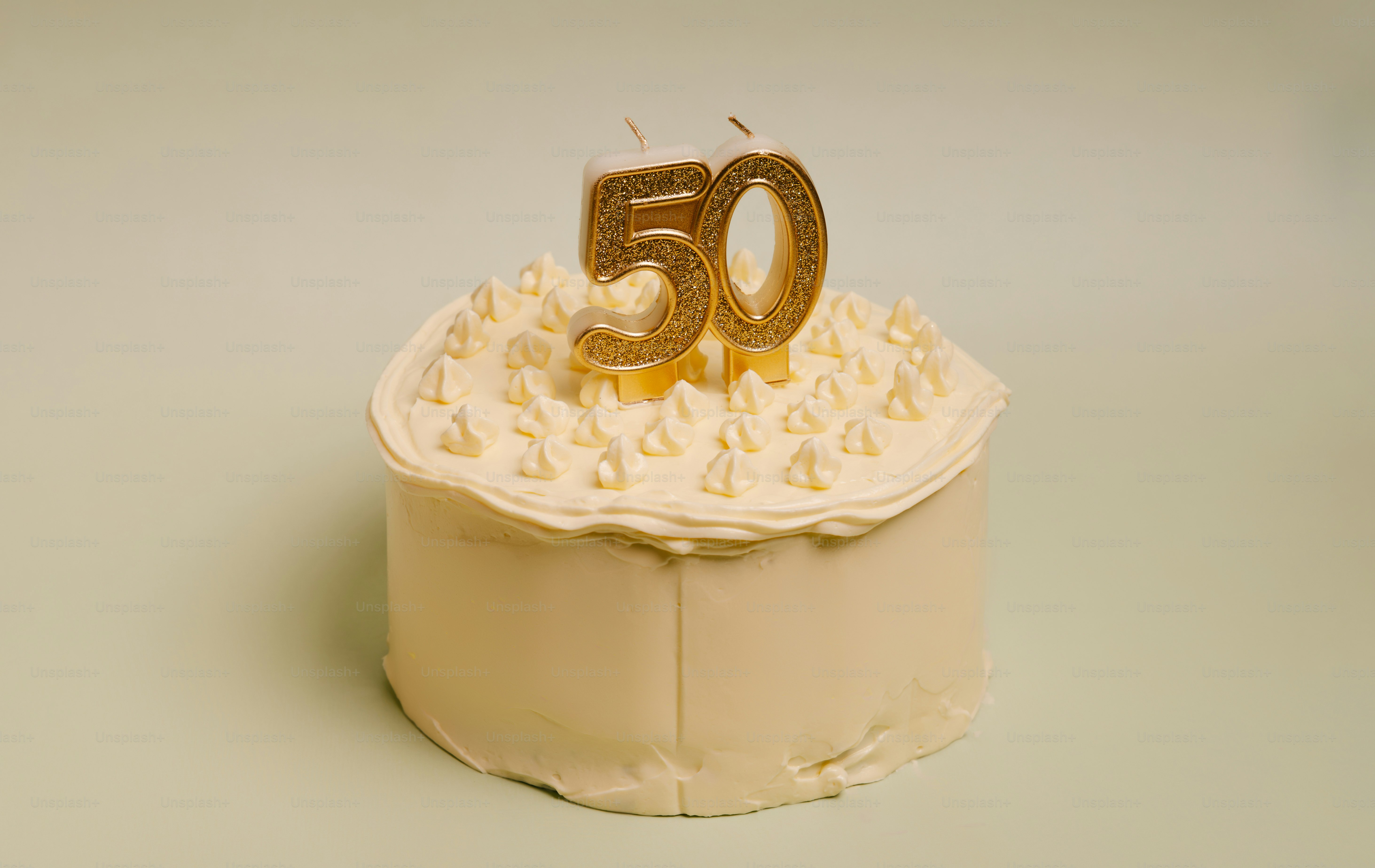 A white frosted cake topped with gold glittery number fifty candles