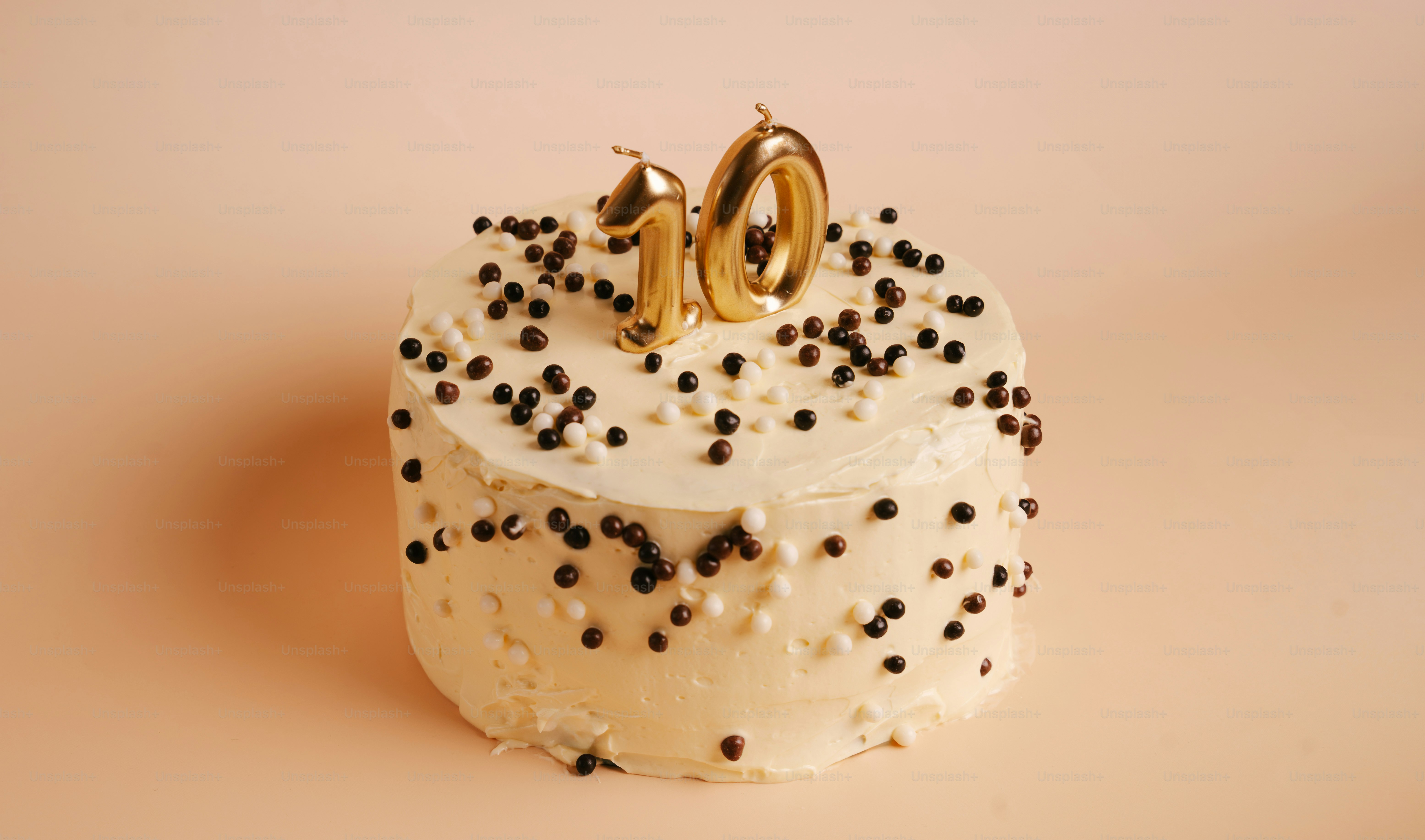 A round cake with white frosting and chocolate sprinkles topped with gold number candles
